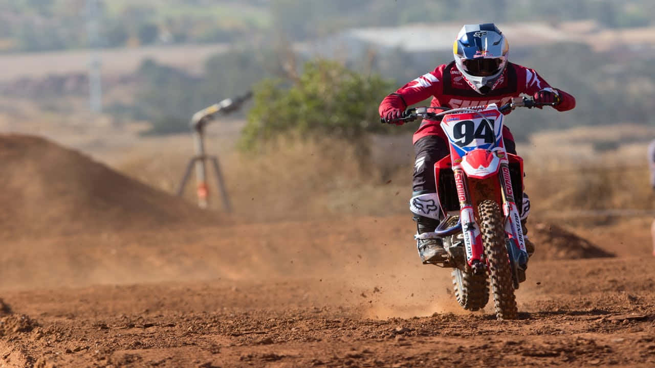 Ken Roczen 紅色越野摩托桌面 壁紙 — 一名身穿紅色裝備的越野電單車手在泥地賽道上傾斜入彎，在明亮的日光下揚起灰塵。