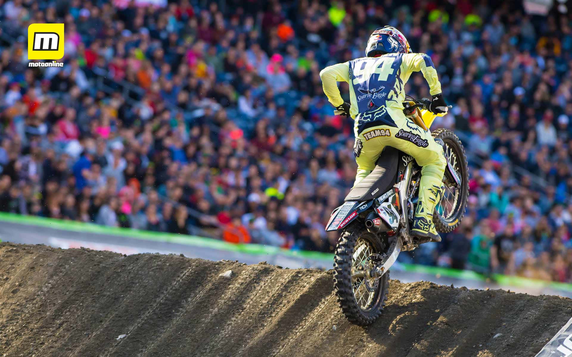 Ken Roczen 與觀眾群的越野賽桌面 壁紙 — 一名身穿黃色裝備的越野電單車手飛越土坡，滿座的體育館觀眾在下方歡呼。