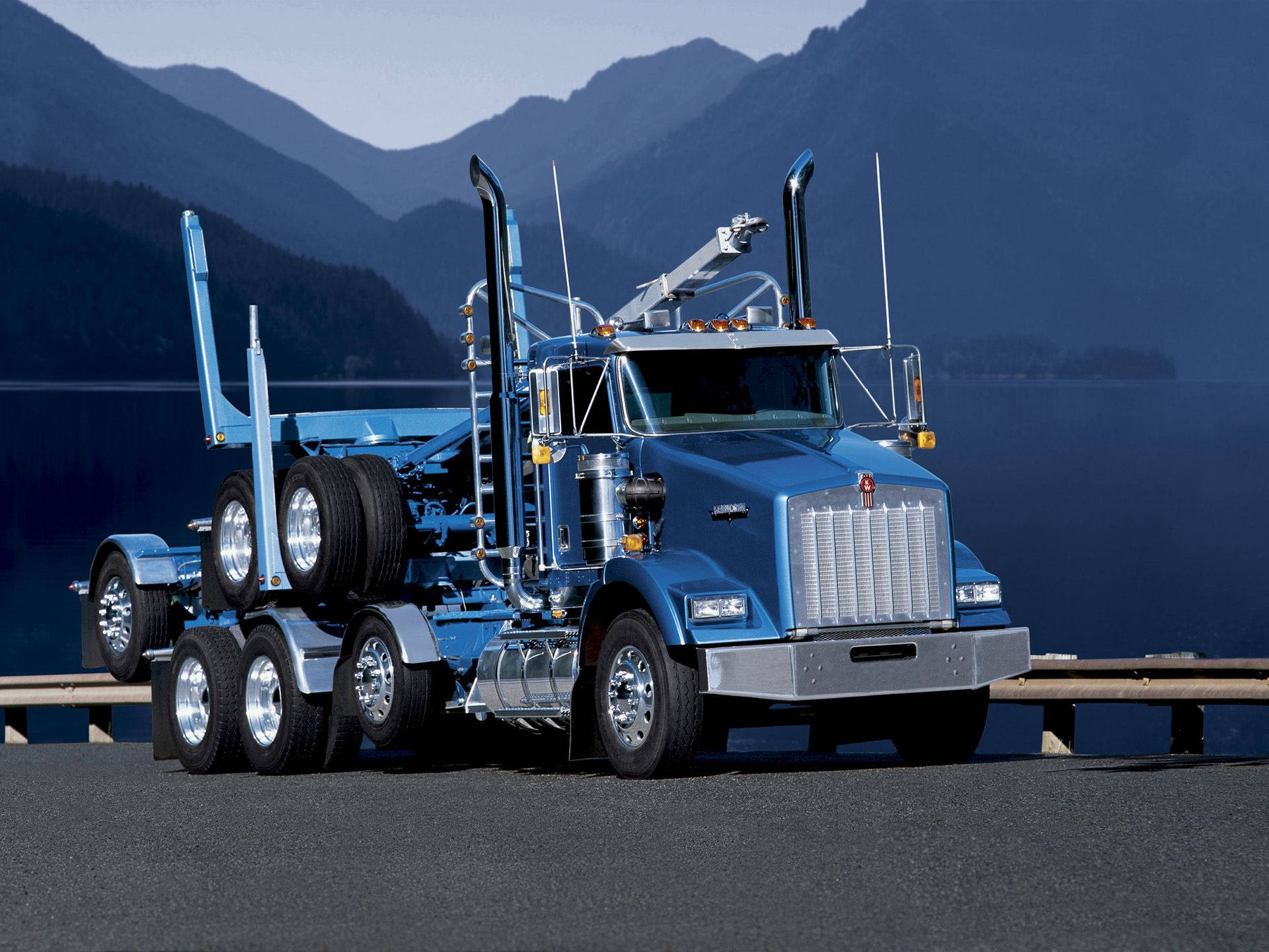 炫目金屬藍Kenworth卡車 壁紙 — 一輛搶眼的藍色 Kenworth 運木車，帶有鍍鉻裝飾，停泊在路邊，俯瞰著晴朗天空下寧靜的山間湖泊。