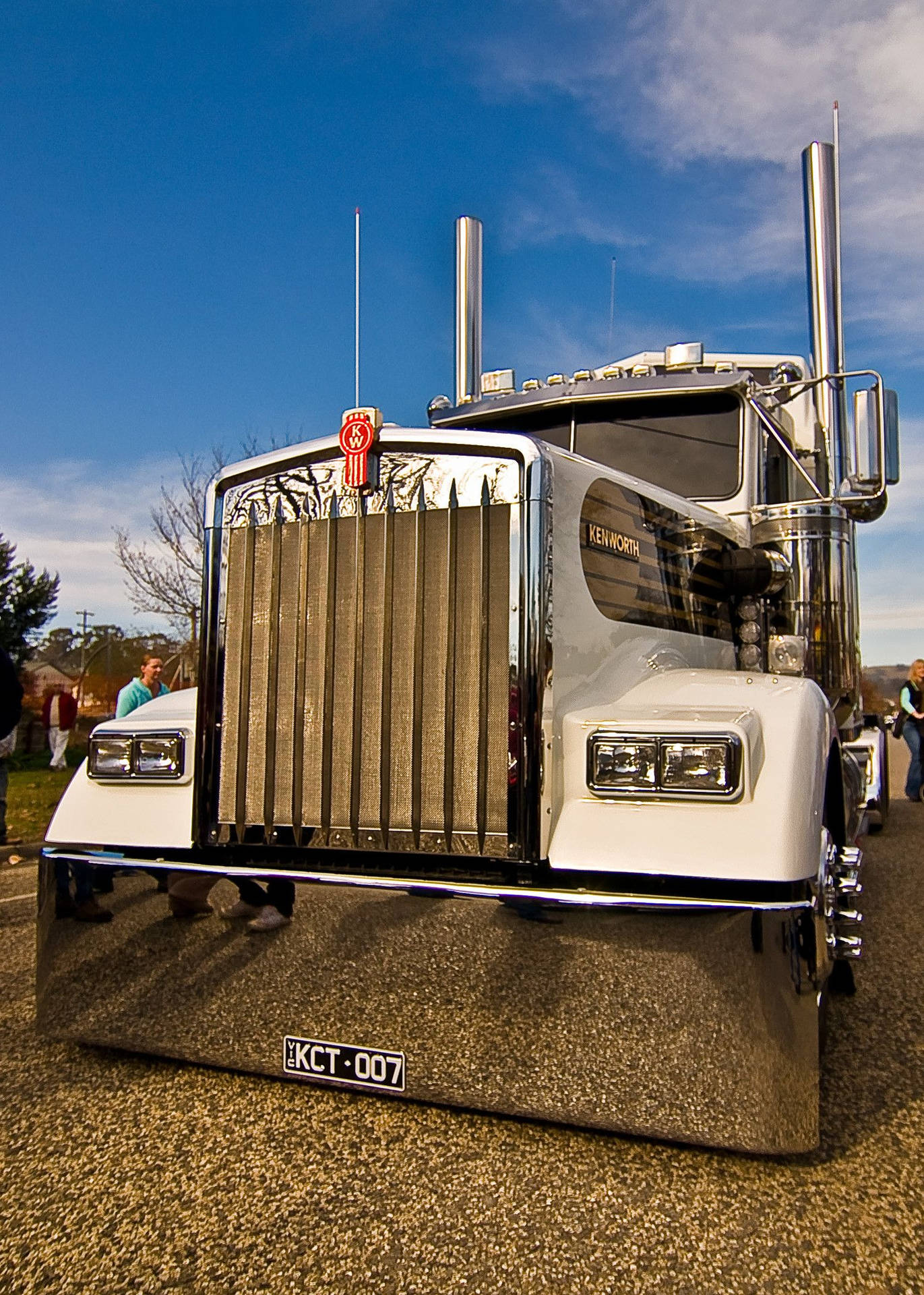 鍍鉻白色Kenworth半掛卡車停在碎石路上，附近有人。