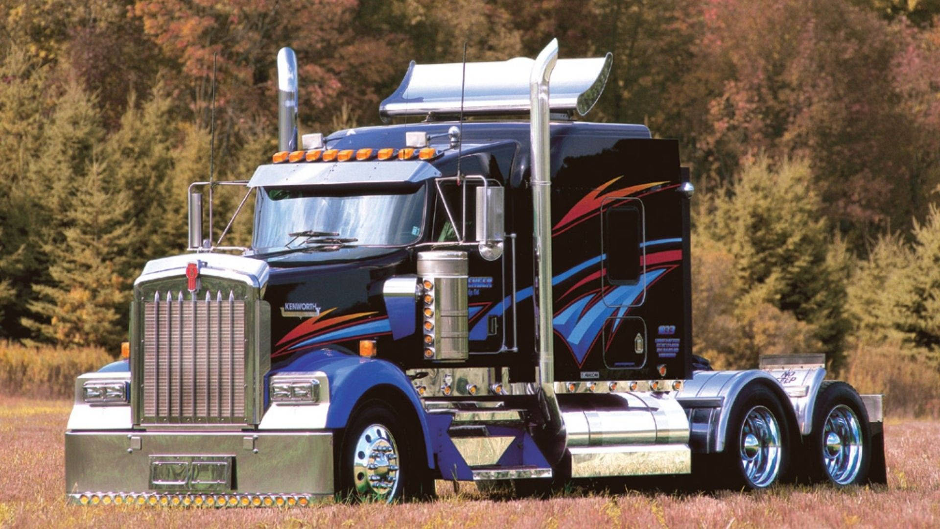 一輛定制噴漆的 Kenworth 半掛卡車停在色彩繽紛的秋林中。