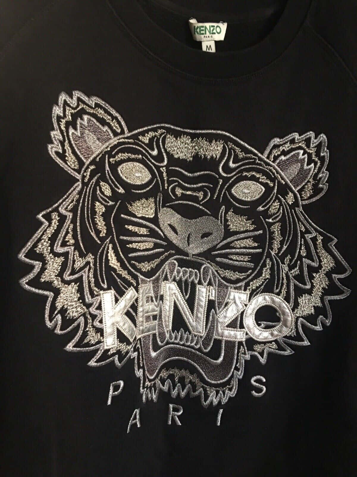 Kenzo男裝漸層虎紋 壁紙 — 黑色 Kenzo 衛衣特寫，帶有精緻的銀色刺繡老虎頭標誌，下方有「KENZO PARIS」字樣。