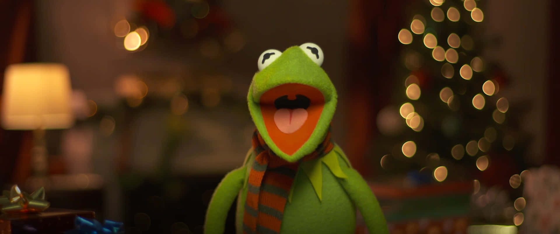 Kermit the Frog 在一個舒適的節日環境中，有聖誕樹和燈。