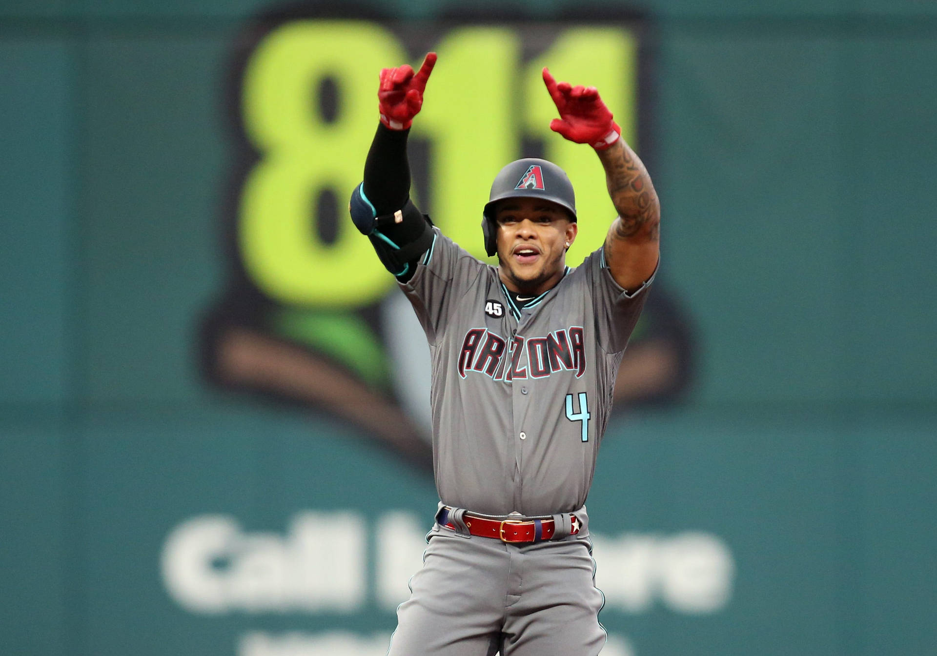 Ketel Marte 一號手勢 壁紙 — 身穿灰色亞利桑那隊服的棒球選手，在綠色牆壁前高舉雙臂，戴著紅色手套，慶祝，牆上有霓虹燈數字811。