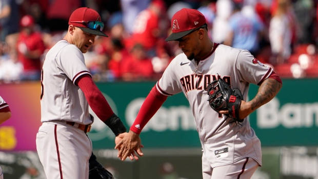 Ketel Marte 低五 壁紙 — 兩名身穿亞利桑那響尾蛇隊球衣的棒球運動員在陽光明媚的球場上握手，身後紅色座位上有球迷。