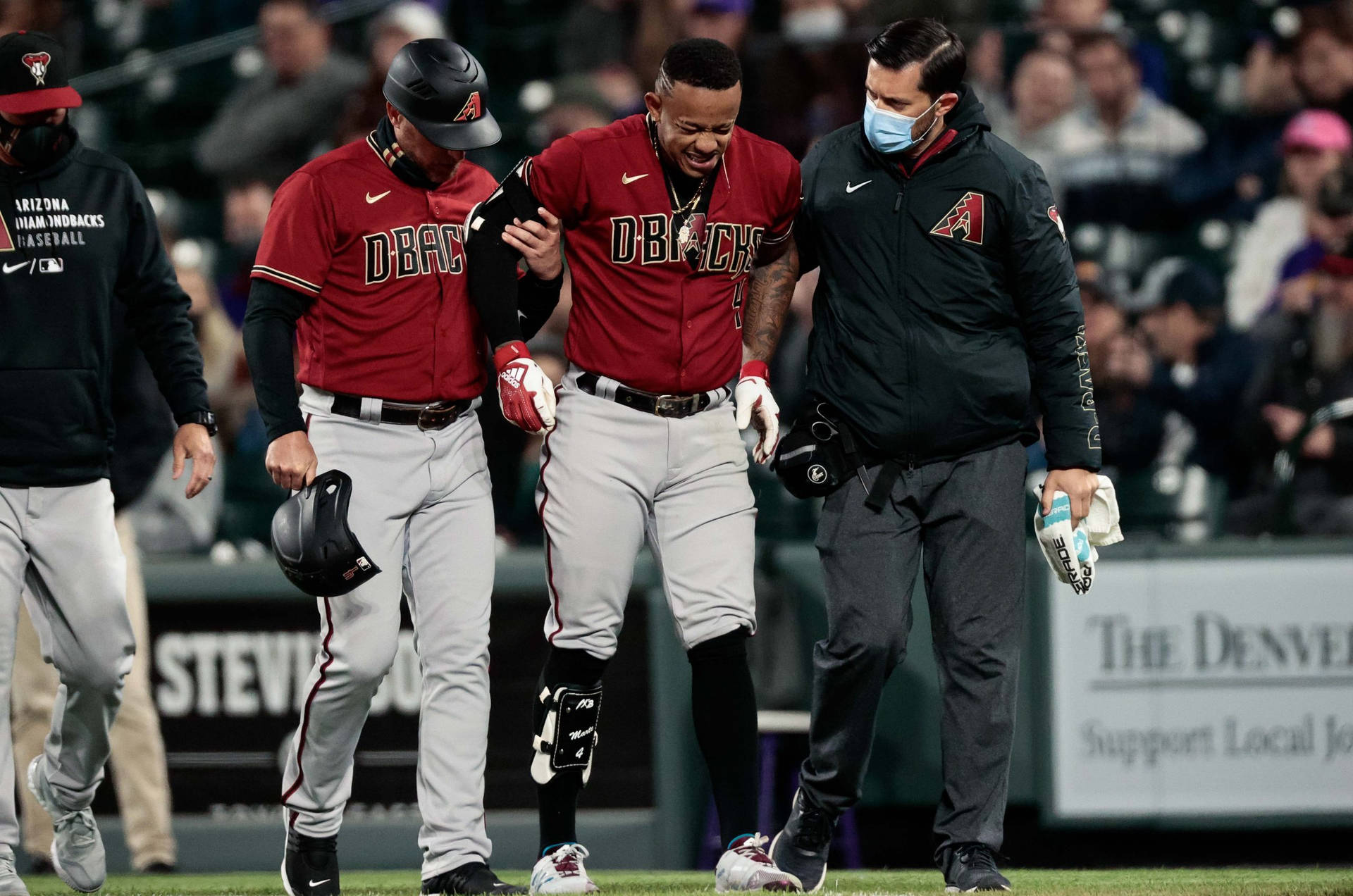 Ketel Marte 受傷 壁紙 — 一名身穿紅灰色球衣的棒球運動員在夜間比賽中受傷後，由隊友和工作人員協助離場。