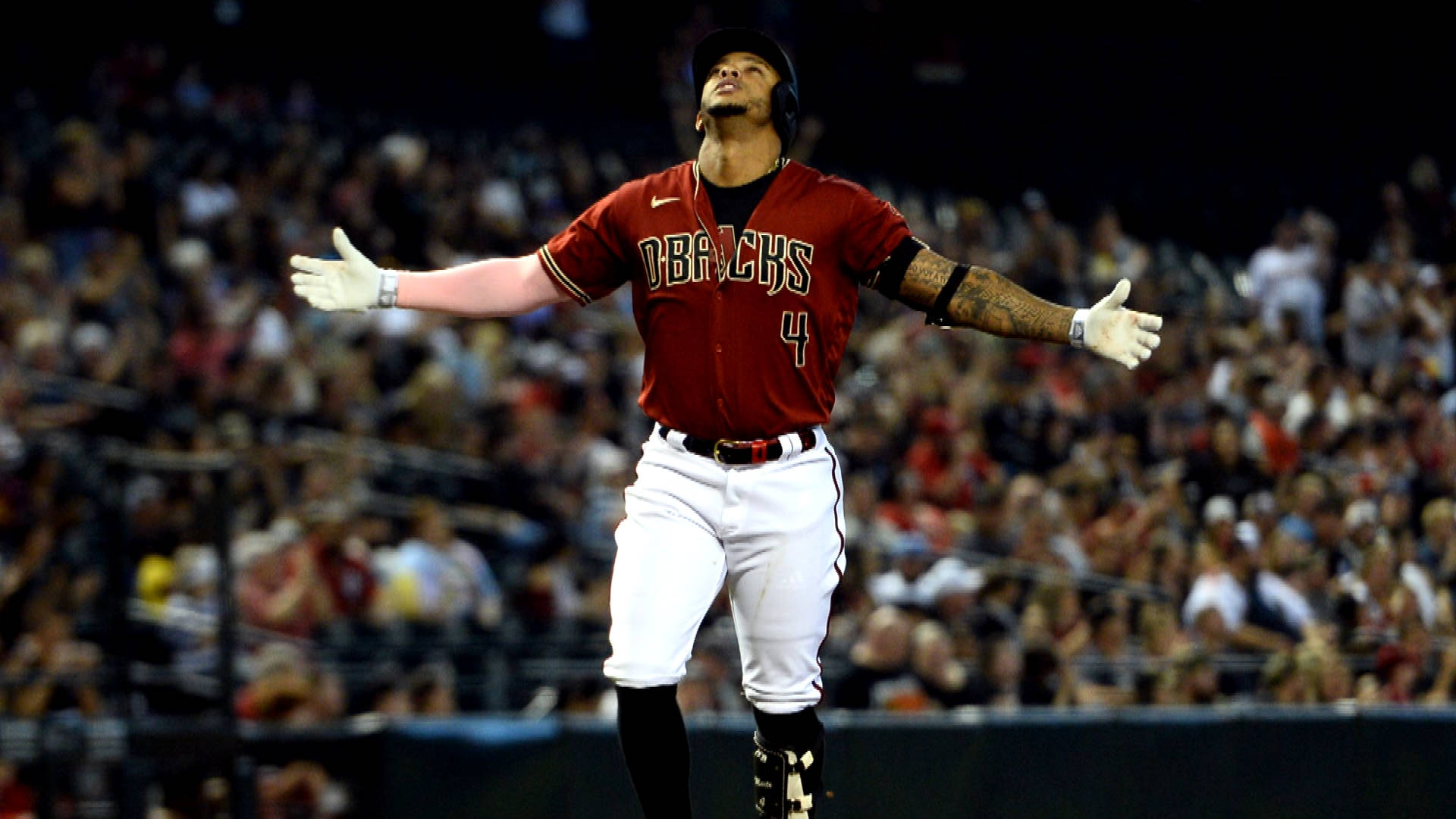 Ketel Marte 張開雙臂 壁紙 — 身穿紅色Diamondbacks球衣的棒球運動員在球場燈光下張開雙臂慶祝。