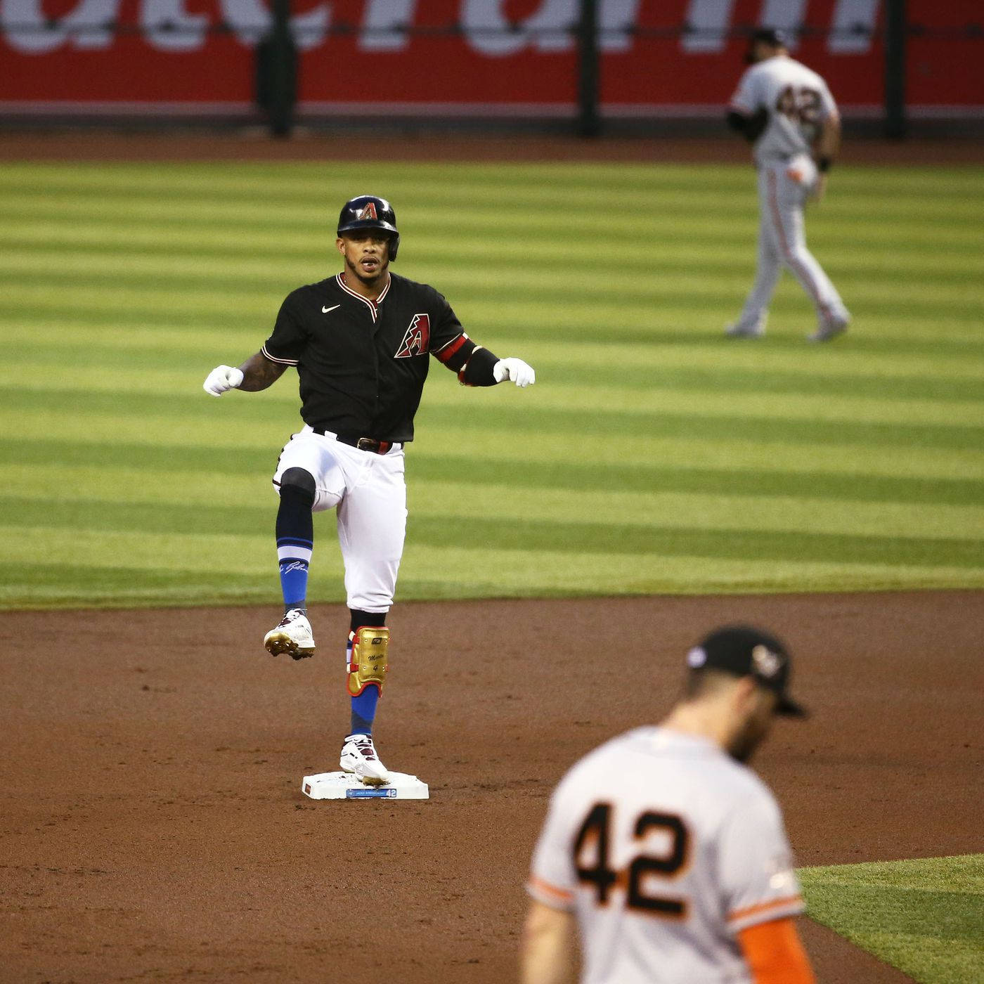 Ketel Marte 黑色球衣 壁紙 — 一名身穿黑色球衣的棒球運動員在夜間比賽中，在壘包上慶祝，球場燈光照亮場地。