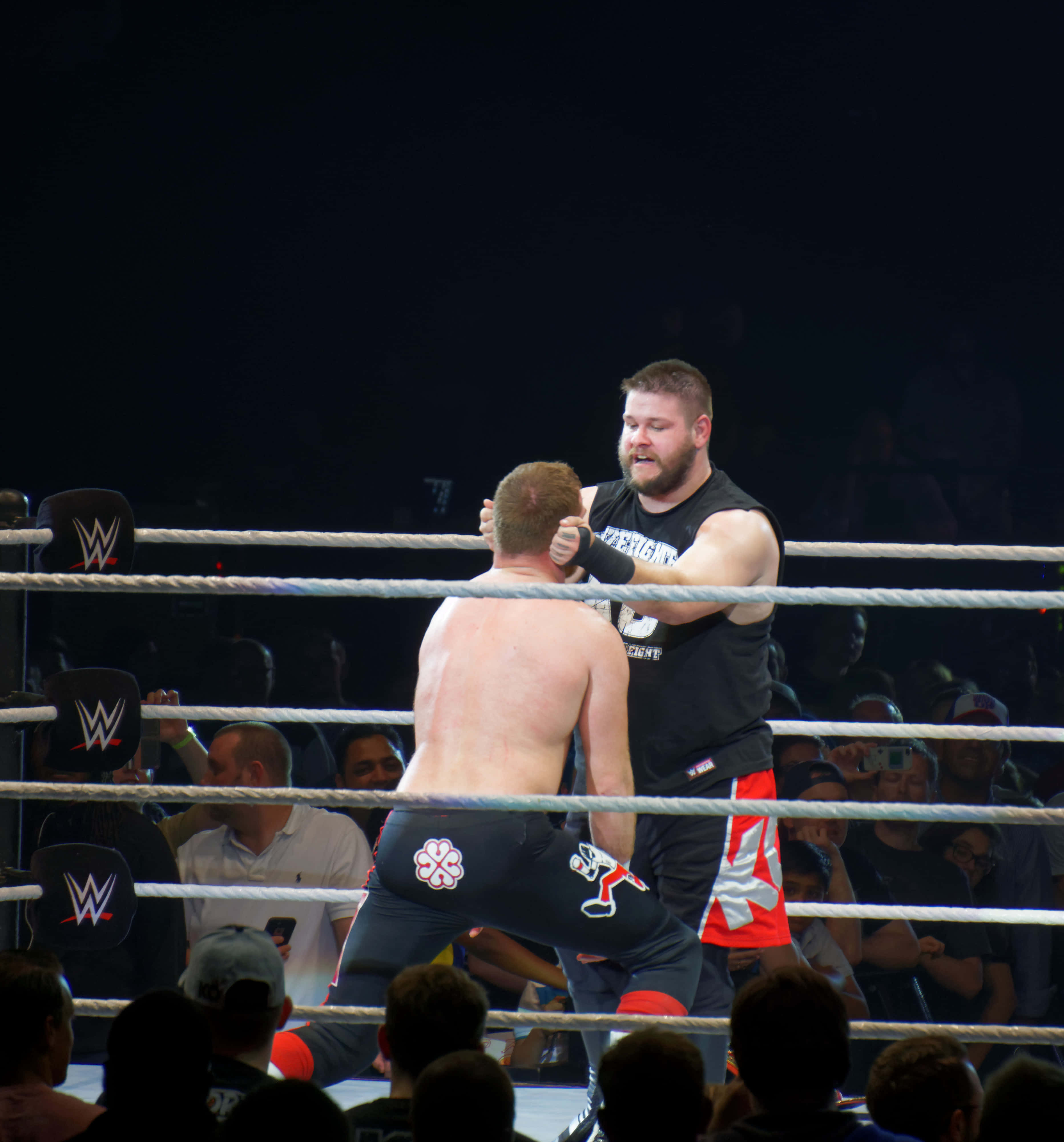 Kevin Owens 與 Sami Zayn WWE 力量對決 壁紙 — 兩名摔角手在燈光明亮的擂台上激烈纏鬥，觀眾在場館燈光下觀看。