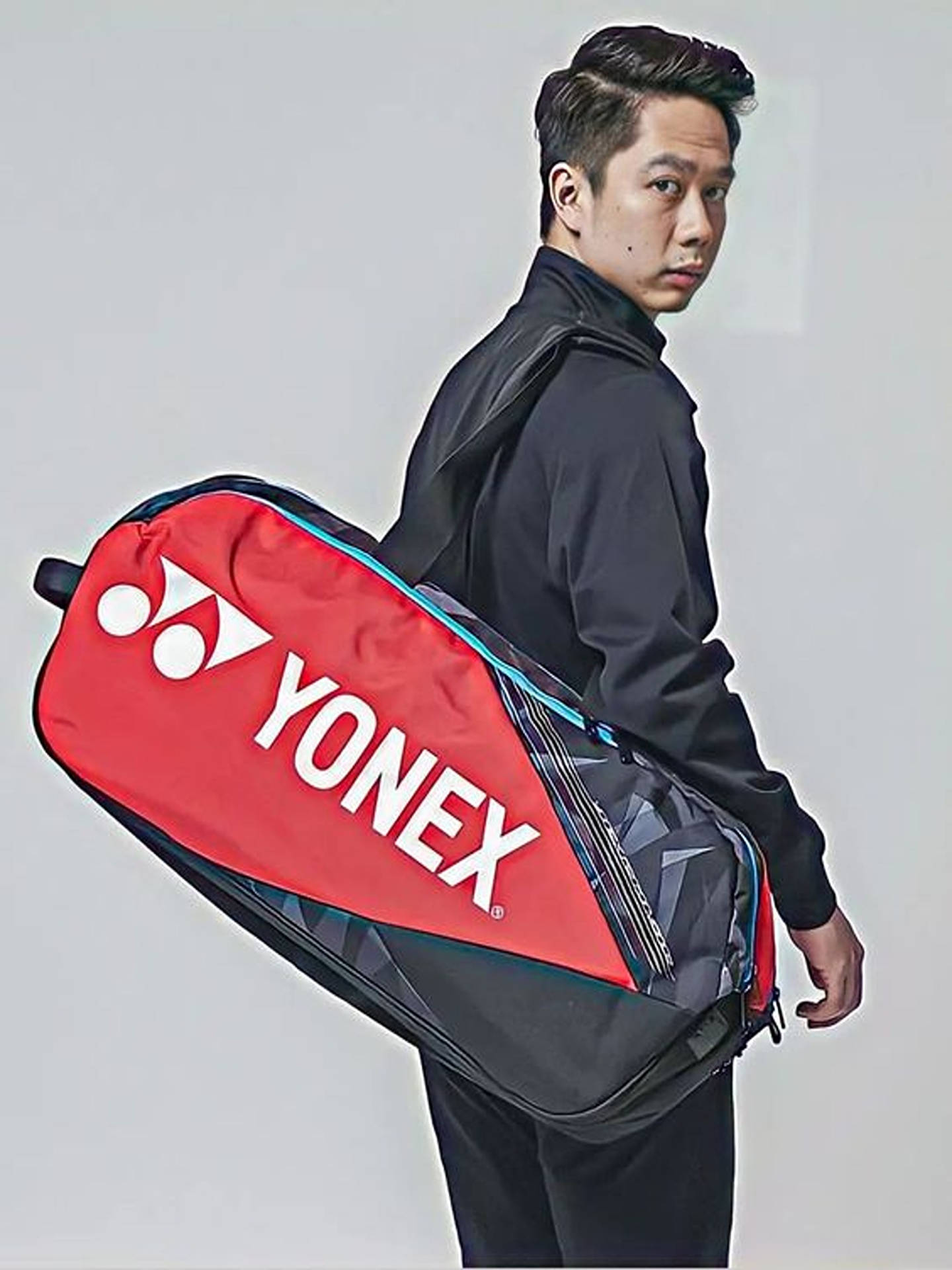 身穿黑色運動服的男子背著一個紅黑相間的Yonex羽毛球袋。