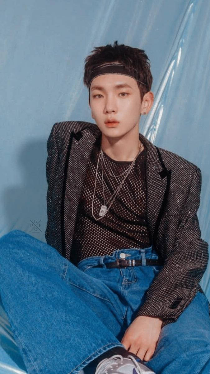 Key Shinee 壁紙 — 一個戴著頭帶的年輕男子，隨意地坐在半透明的藍色背景前，穿著圖案西裝外套和牛仔褲。