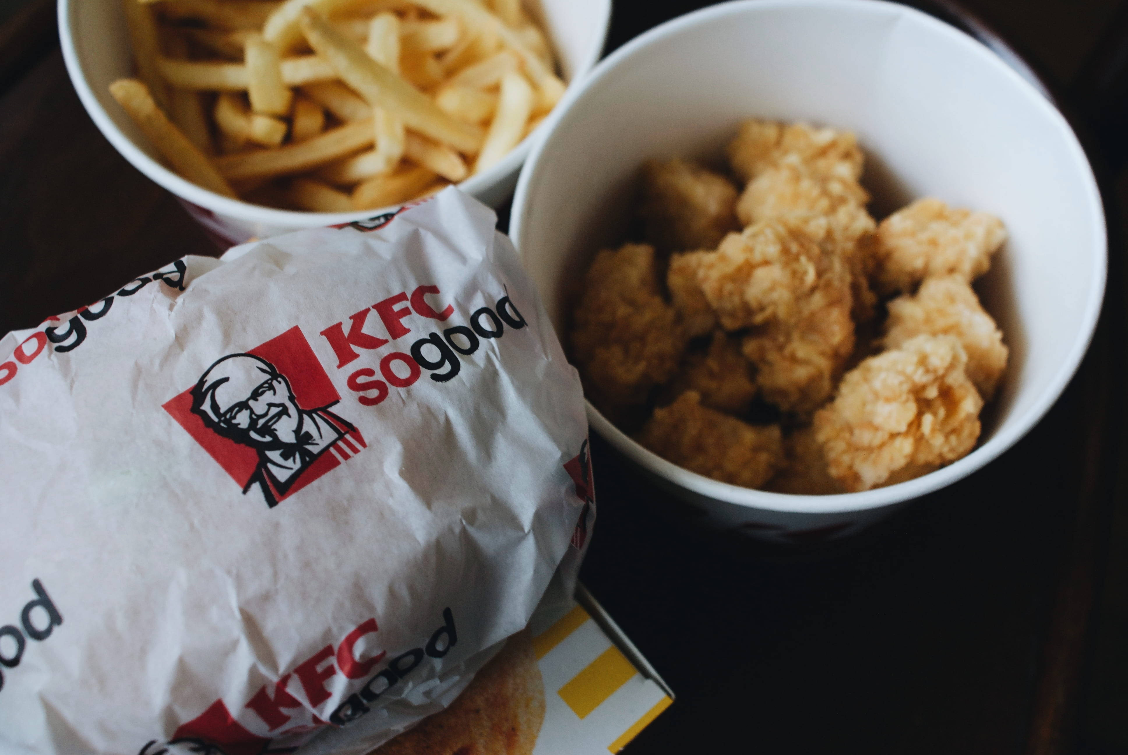 KFC套餐美食 壁紙 — KFC 餐點的近距離特寫，包括酥脆的炸雞塊和金黃色薯條，放在品牌紙張和碗中。