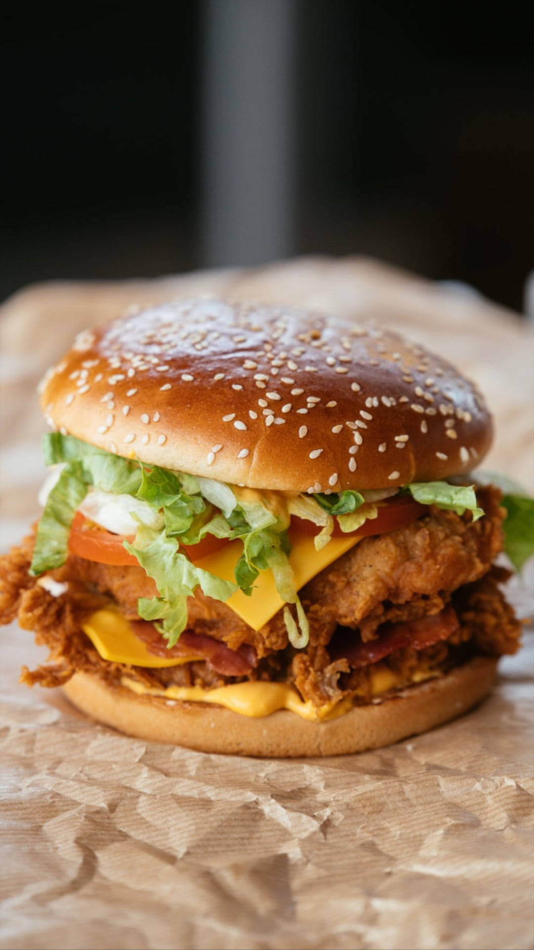 KFC炸雞堡 壁紙 — 一個多汁的炸雞漢堡，配上融化芝士、煙肉、番茄和生菜，放在芝麻麵包上，置於皺巴巴的棕色紙上。