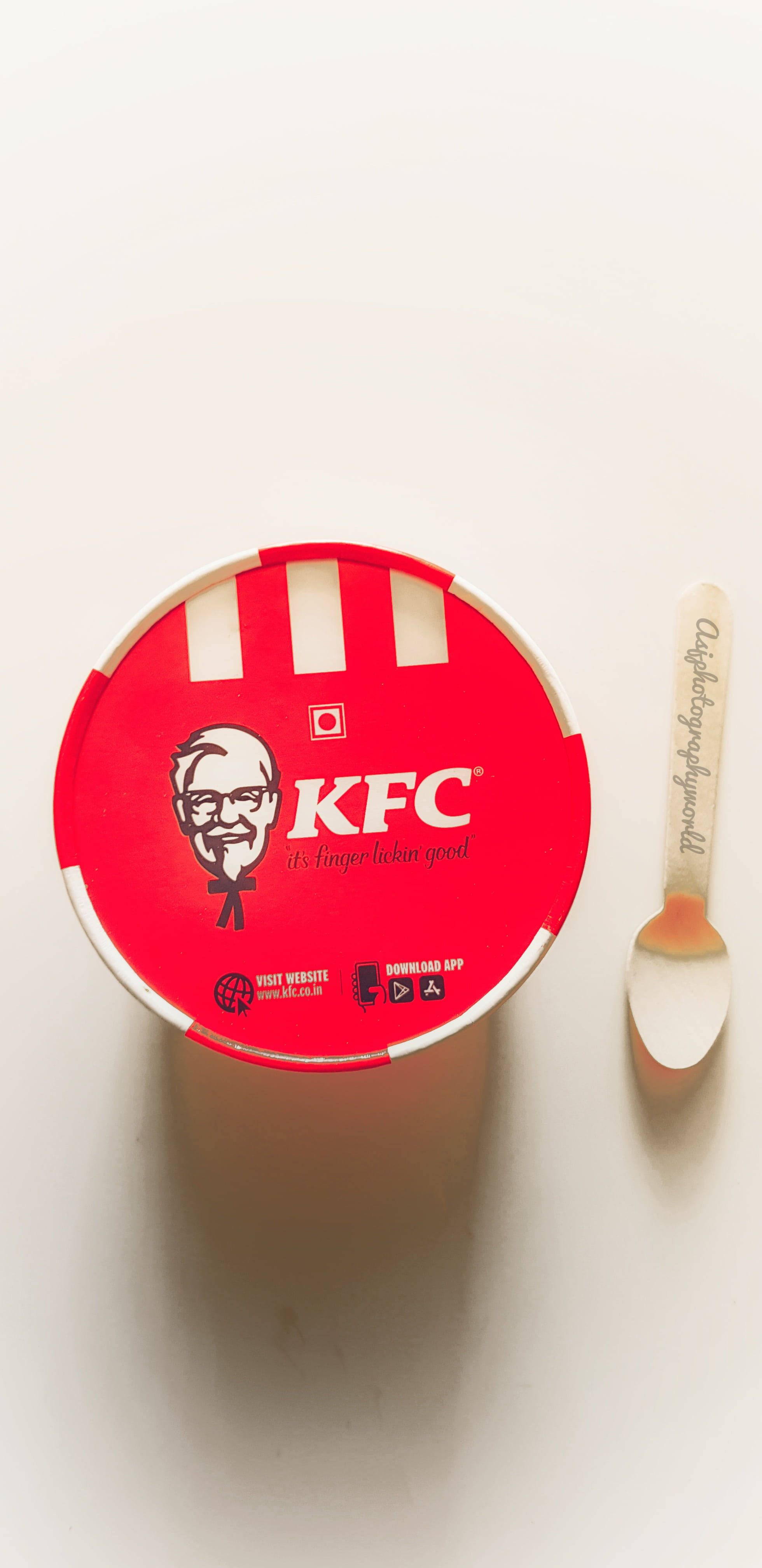 KFC雞桶 壁紙 — 一個紅色KFC桶，上面有山德士上校標誌和品牌湯匙，放在純白色表面上，從正上方俯瞰的視角。