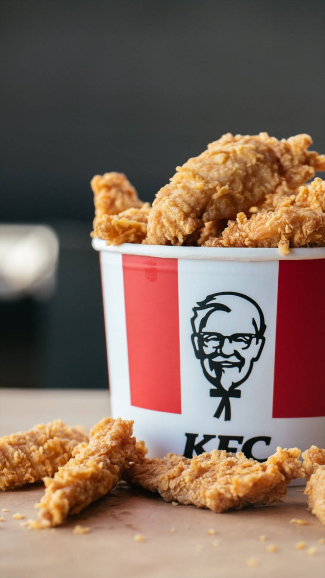 KFC炸雞桶 壁紙 — 金黃酥脆的炸雞塊從經典紅白配色的KFC桶中灑出，背景為深色。