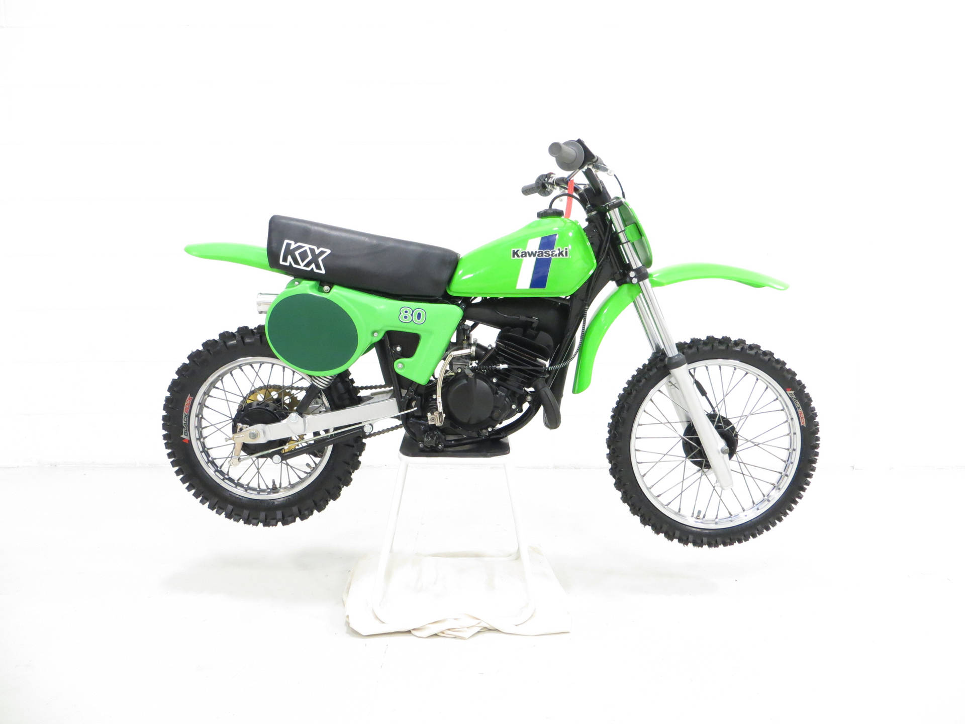鮮綠色Kawasaki KX80越野電單車喺白色展示支架上。