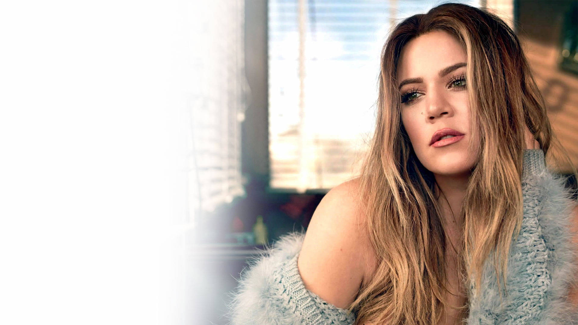 Khloe Kardashian 身穿灰色毛衣 壁紙 — 一位長金髮的女性在窗邊穿著毛絨絨的淺藍色毛衣，若有所思地凝視著。