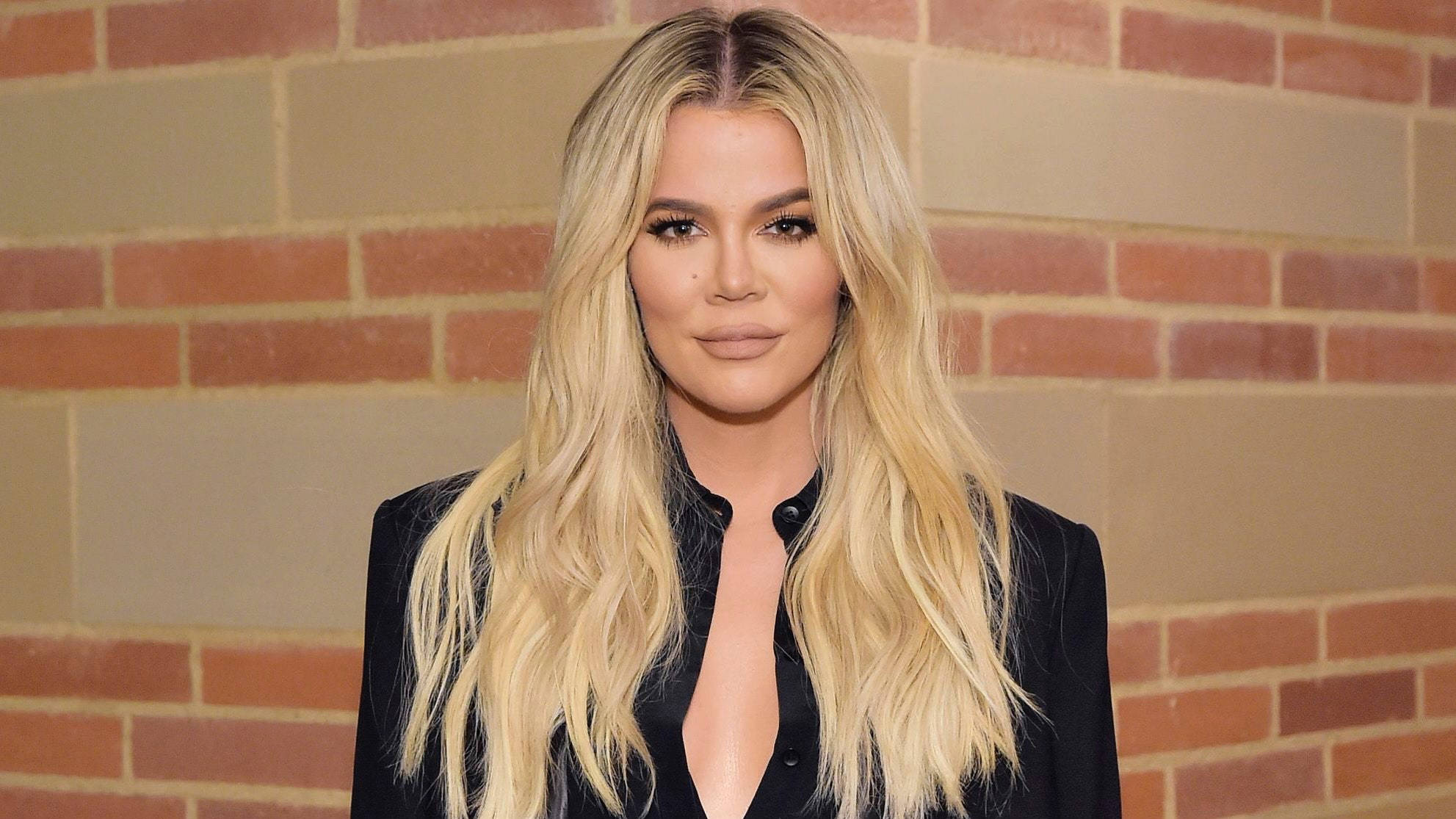 Khloe Kardashian 對磚牆背景 壁紙 — Khloé Kardashian 留著金色長髮，身穿黑色上衣，背景是磚牆。