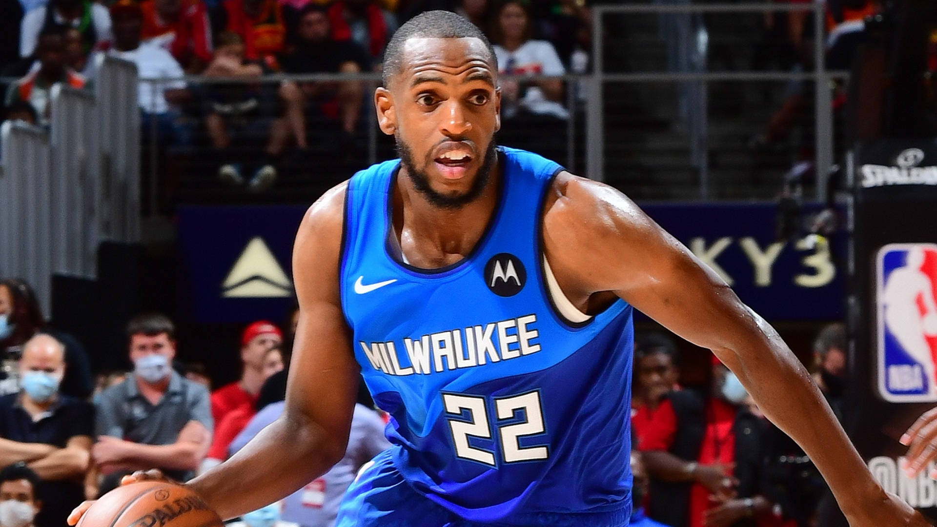 Khris Middleton 藍色戰袍 壁紙 — 一位身穿藍色球衣的密爾沃基公鹿籃球運動員在比賽中激烈運球，背景有觀眾。