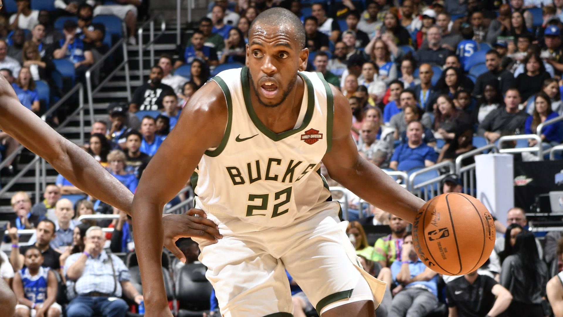 Khris Middleton Bucks 球員 壁紙 — 一位身穿白色和綠色球衣的密爾沃基公鹿籃球運動員在擠滿觀眾的場館中運球，同時被防守。