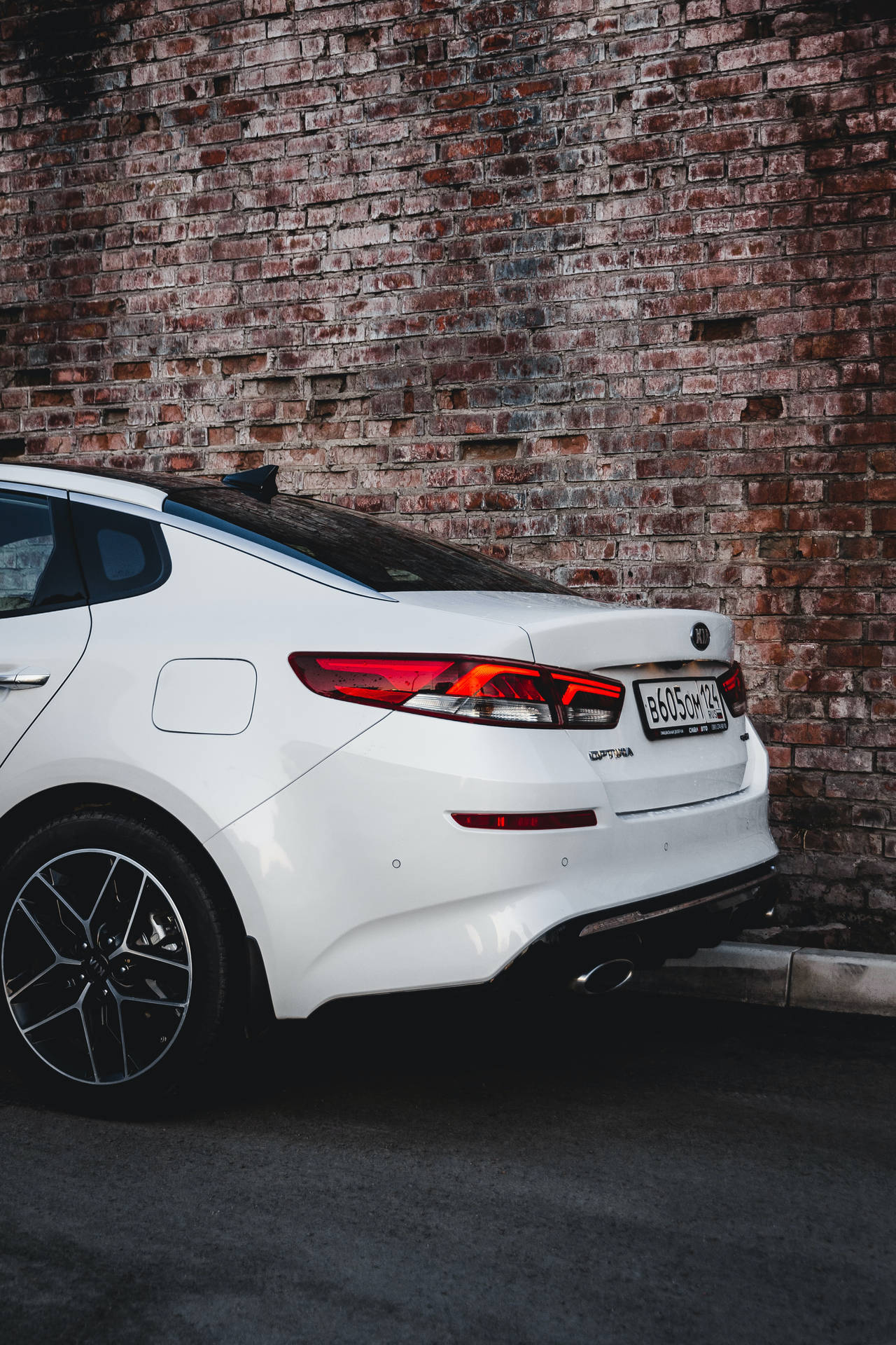 白色Kia Stinger夜間停泊在磚牆旁。