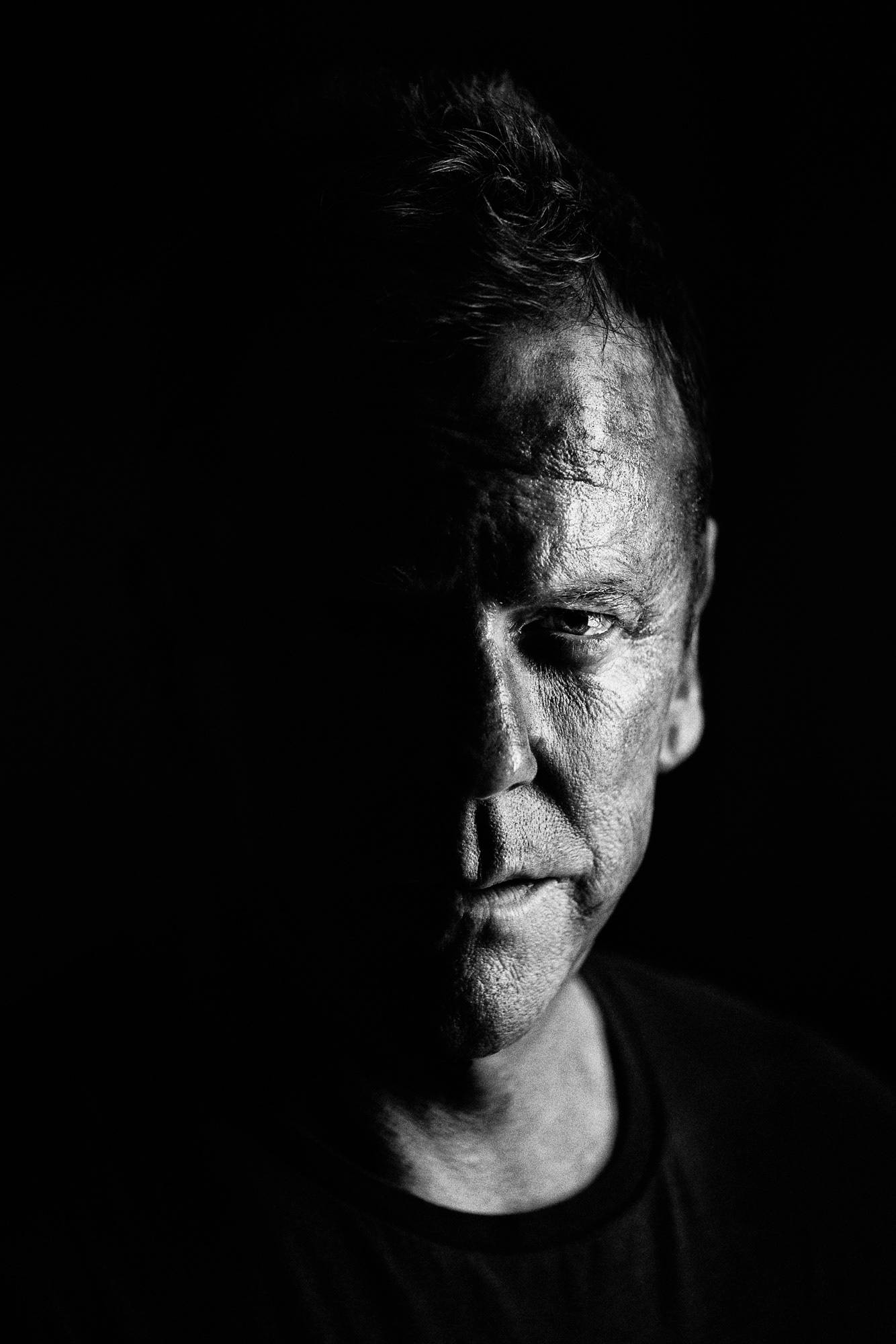 Kiefer Sutherland 飾演 Jack Bauer 黑白肖像 壁紙 — 一張高對比度的黑白人像，男人的臉一半在陰影中，眼神強烈地直視前方。