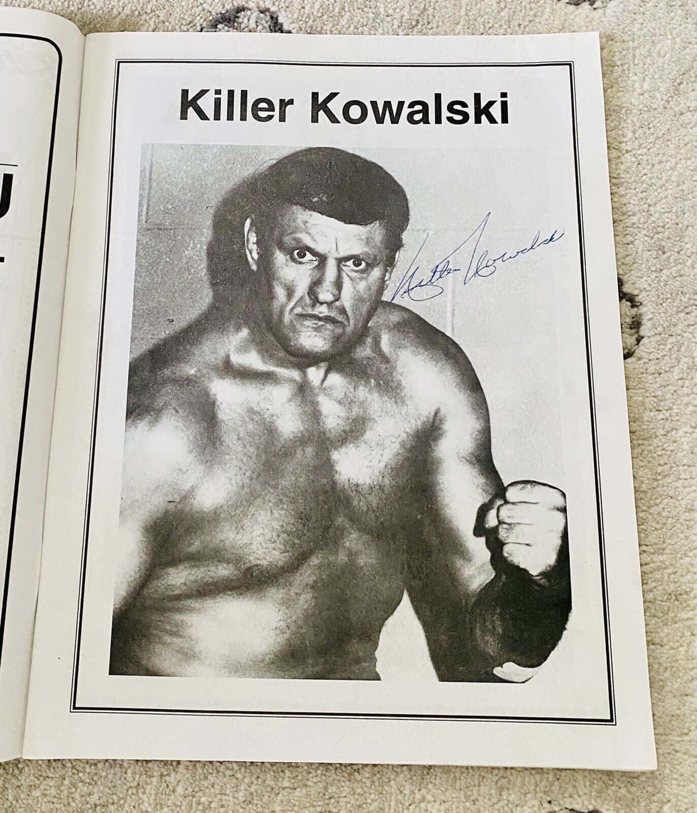 傳奇加拿大摔角手 Killer Kowalski 壁紙 — 一張黑白簽名照片，摔角手Killer Kowalski在地毯上打開的書本內擺出威嚇姿勢。