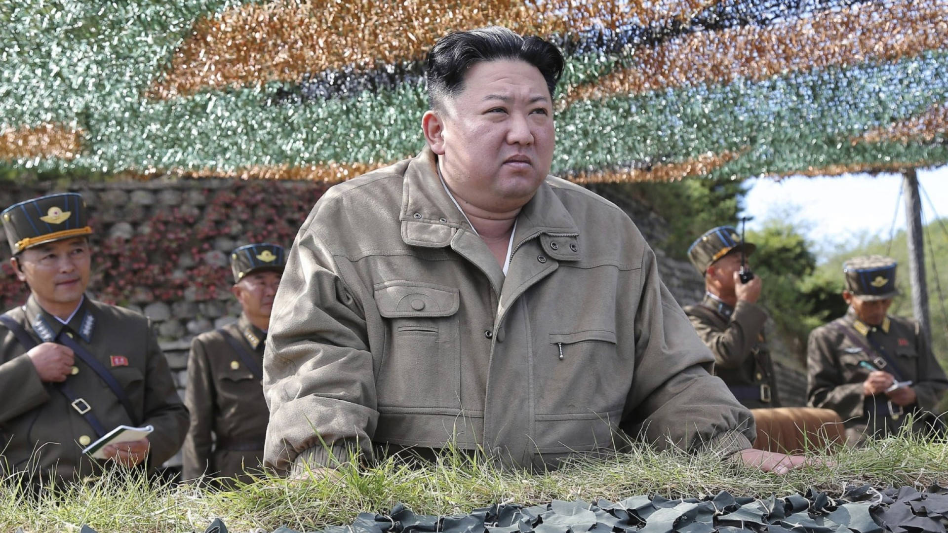 金正恩在戶外與身穿軍服的軍人坐在一起。