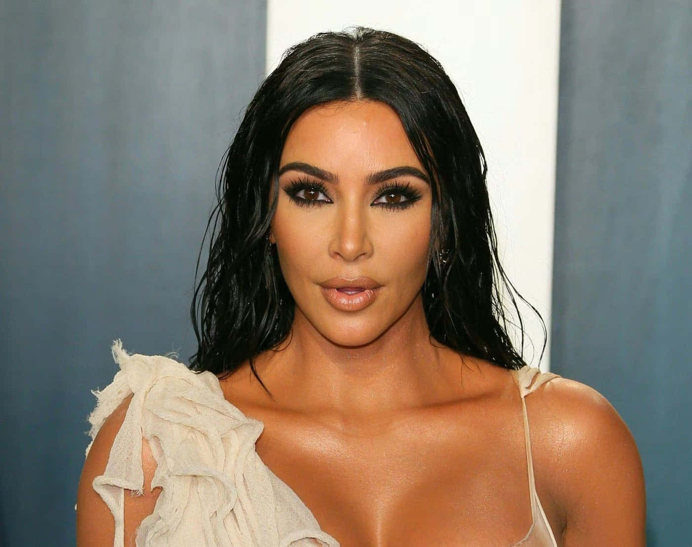 金·卡戴珊 桌布 壁紙 — Kim Kardashian 以濕黑髮和鮮豔妝容在藍白背景前擺姿勢。