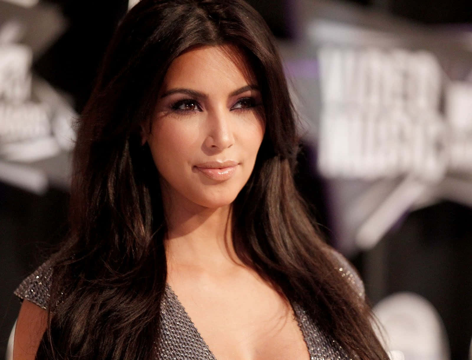 Kim Kardashian 桌布 壁紙 — Kim Kardashian 喺模糊背景標牌嘅紅地毯活動上，自信地穿著閃亮銀色連身裙擺姿勢。