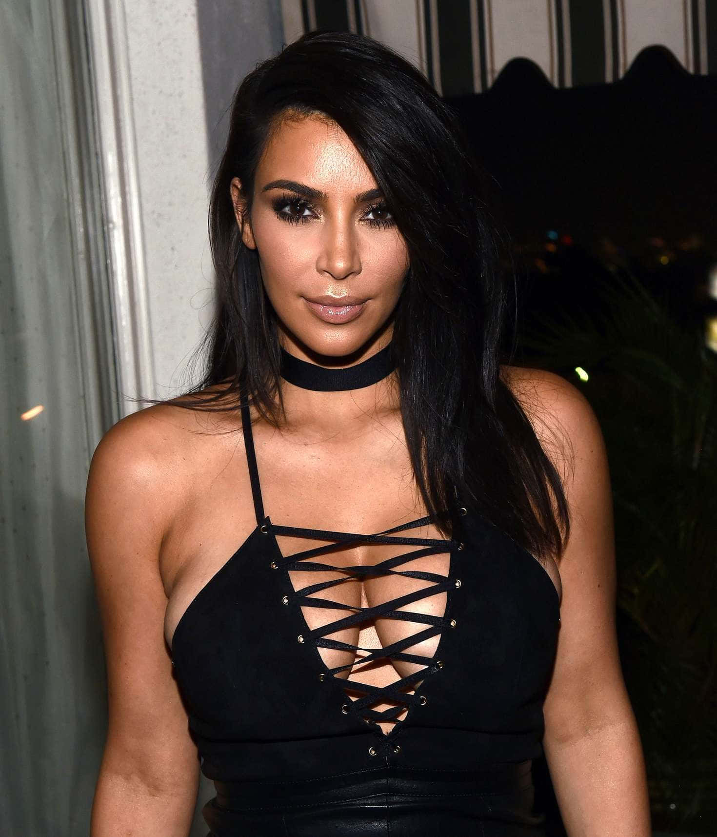 Kim Kardashian 桌布 壁紙 — Kim Kardashian 身穿黑色繫帶上衣和頸鏈，在昏暗的室內背景下擺姿勢。