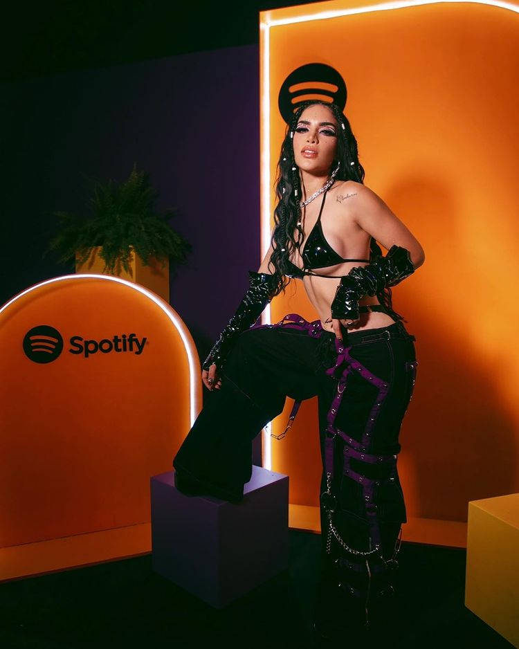 穿著前衛黑紫色服裝的女性在Spotify活動中，在發光的橙色牆前擺姿勢。