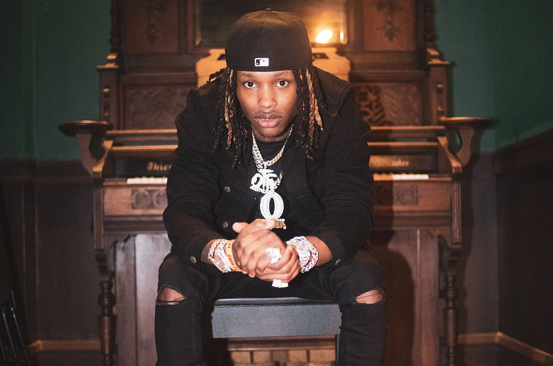 年輕男子留著辮子頭、戴著金鏈，坐在一部復古鋼琴上。