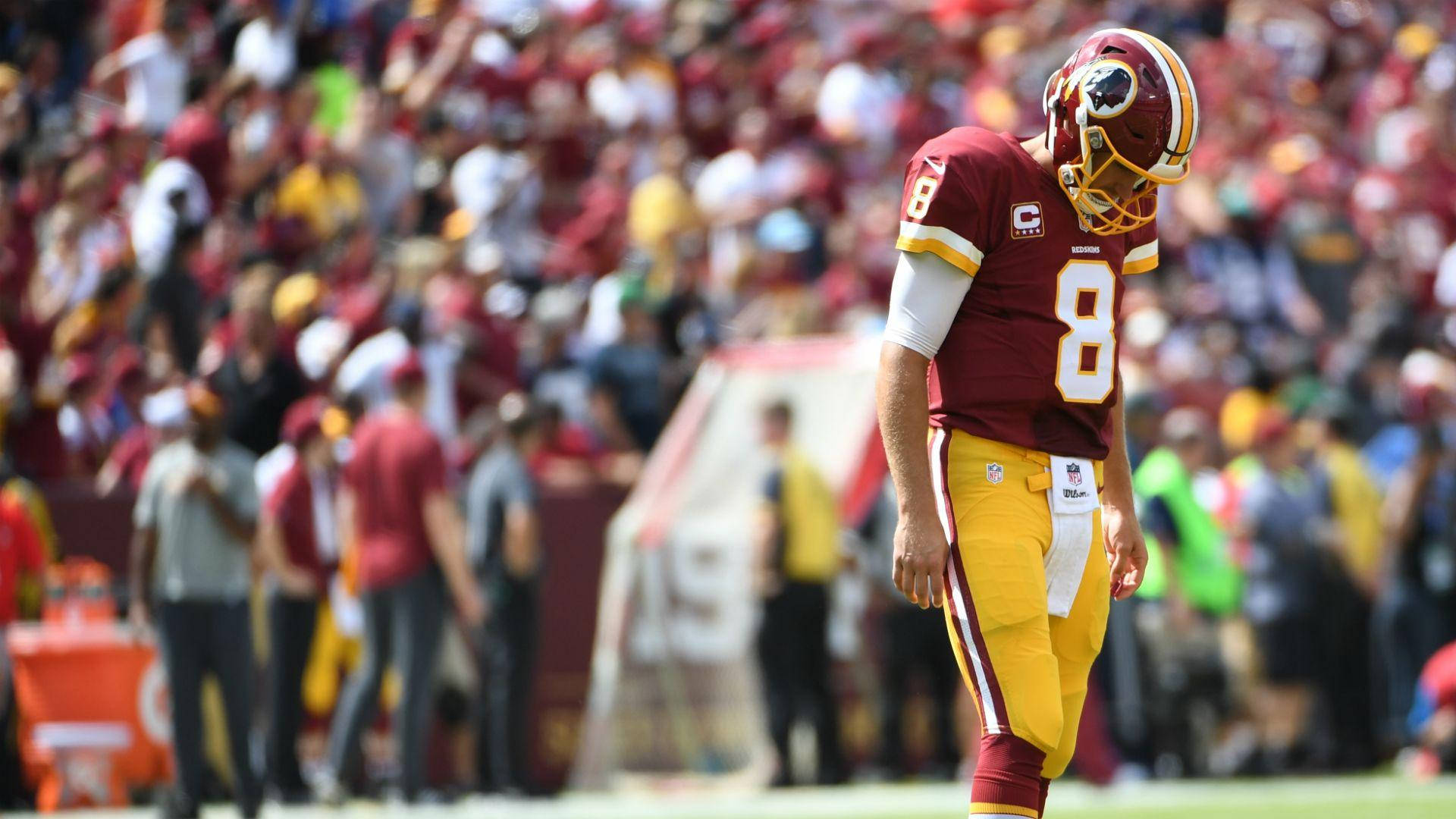 Kirk Cousins 低頭離場 壁紙 — 華盛頓美式足球隊的四分衛身穿棗紅色和金色球衣，在陽光明媚的比賽中低頭沮喪地站在球場上。