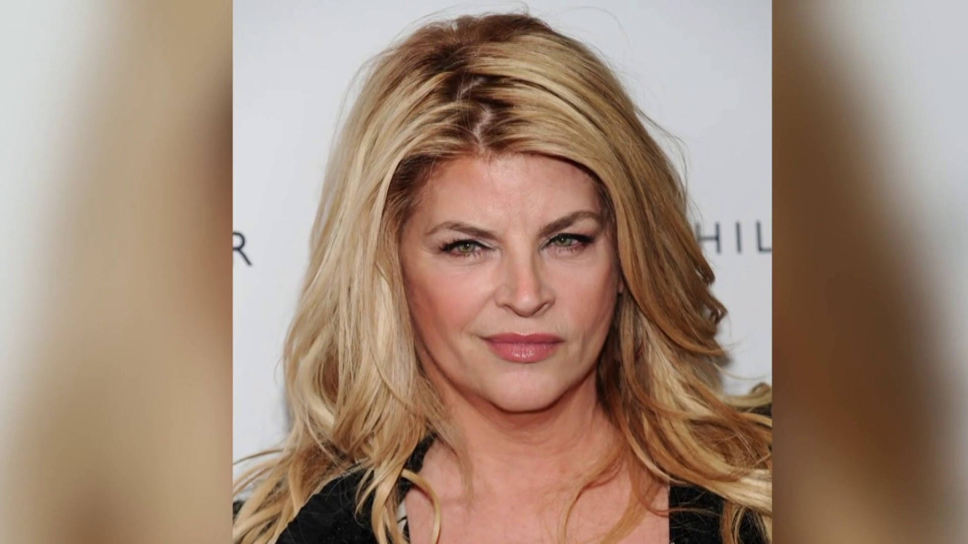 美國女星 Kirstie Alley 紅毯造型 壁紙 — 一個特寫肖像，一位擁有豐盈金髮和含蓄微笑的女性，背景是模糊的白色。