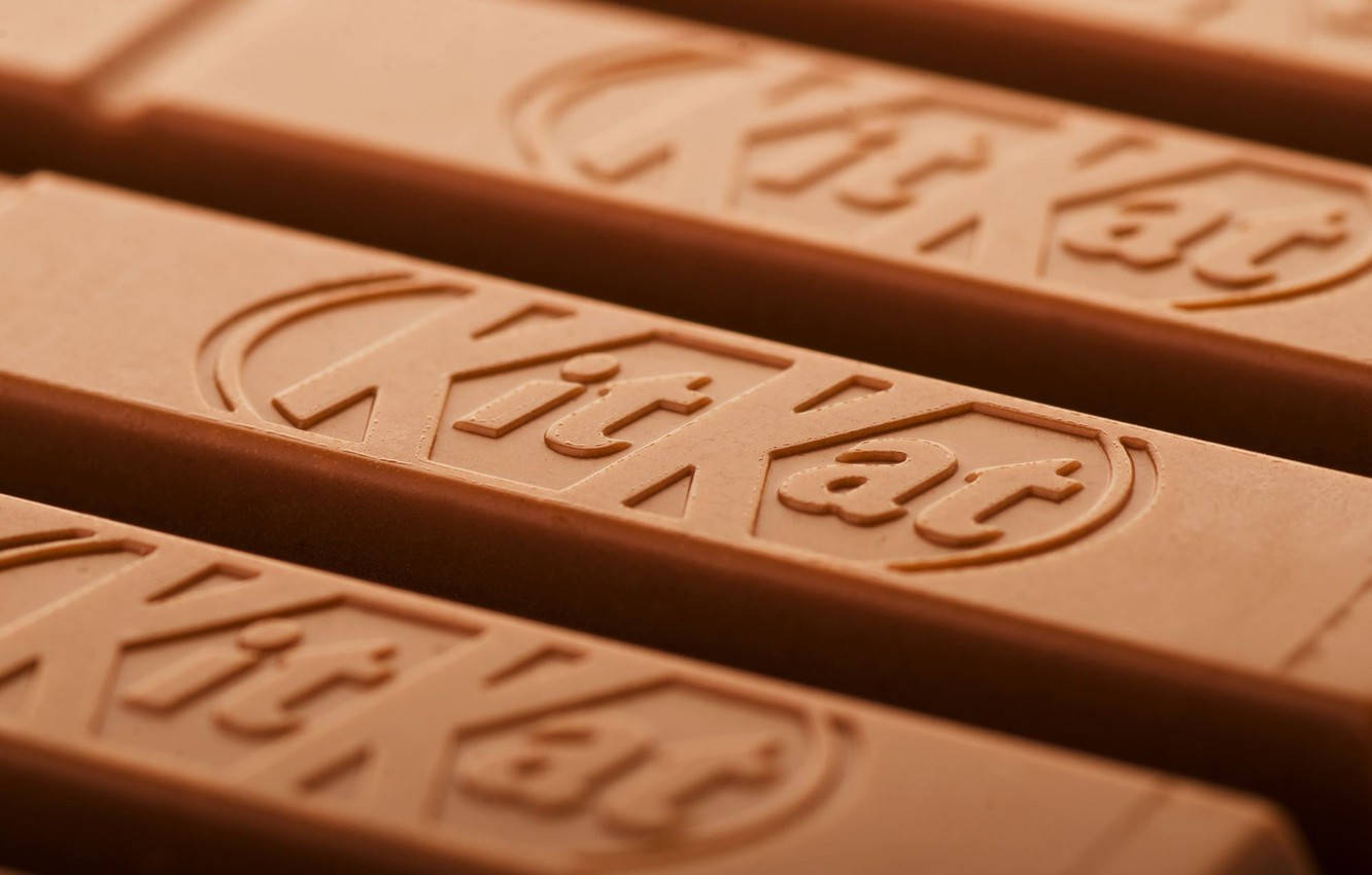Kit Kat 巧克力棒 壁紙 — KitKat 朱古力棒的近鏡，展示壓花標誌，帶有溫暖的棕色色調和柔和光線。