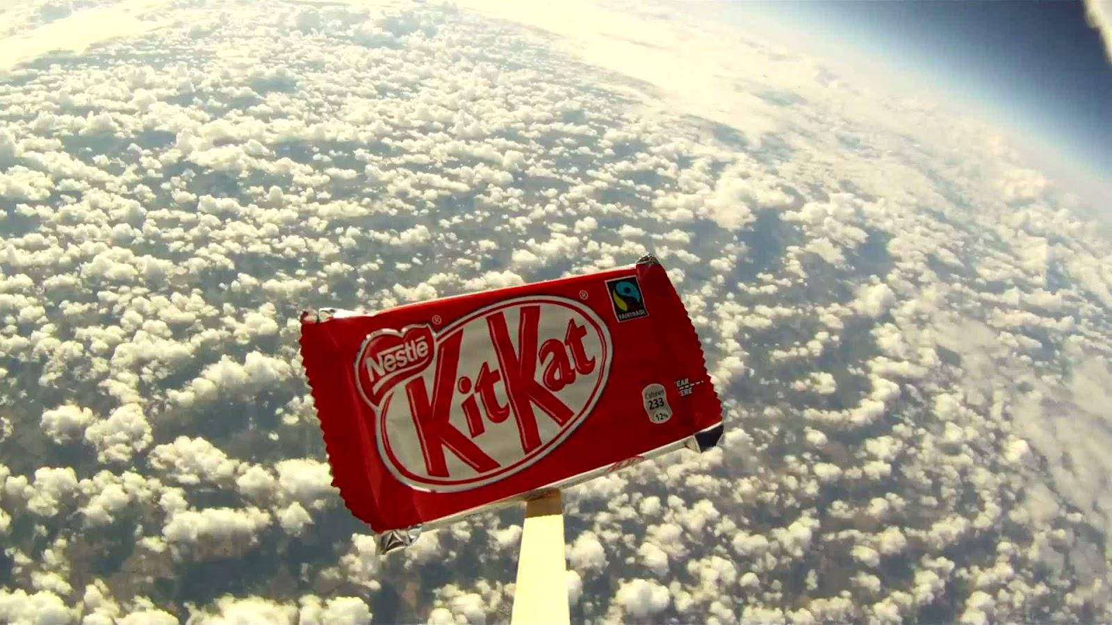 Kit Kat 持於雲朵之上 壁紙 — 一條紅色KitKat在彎曲的藍色地球上，漂浮在蓬鬆的白雲之上。