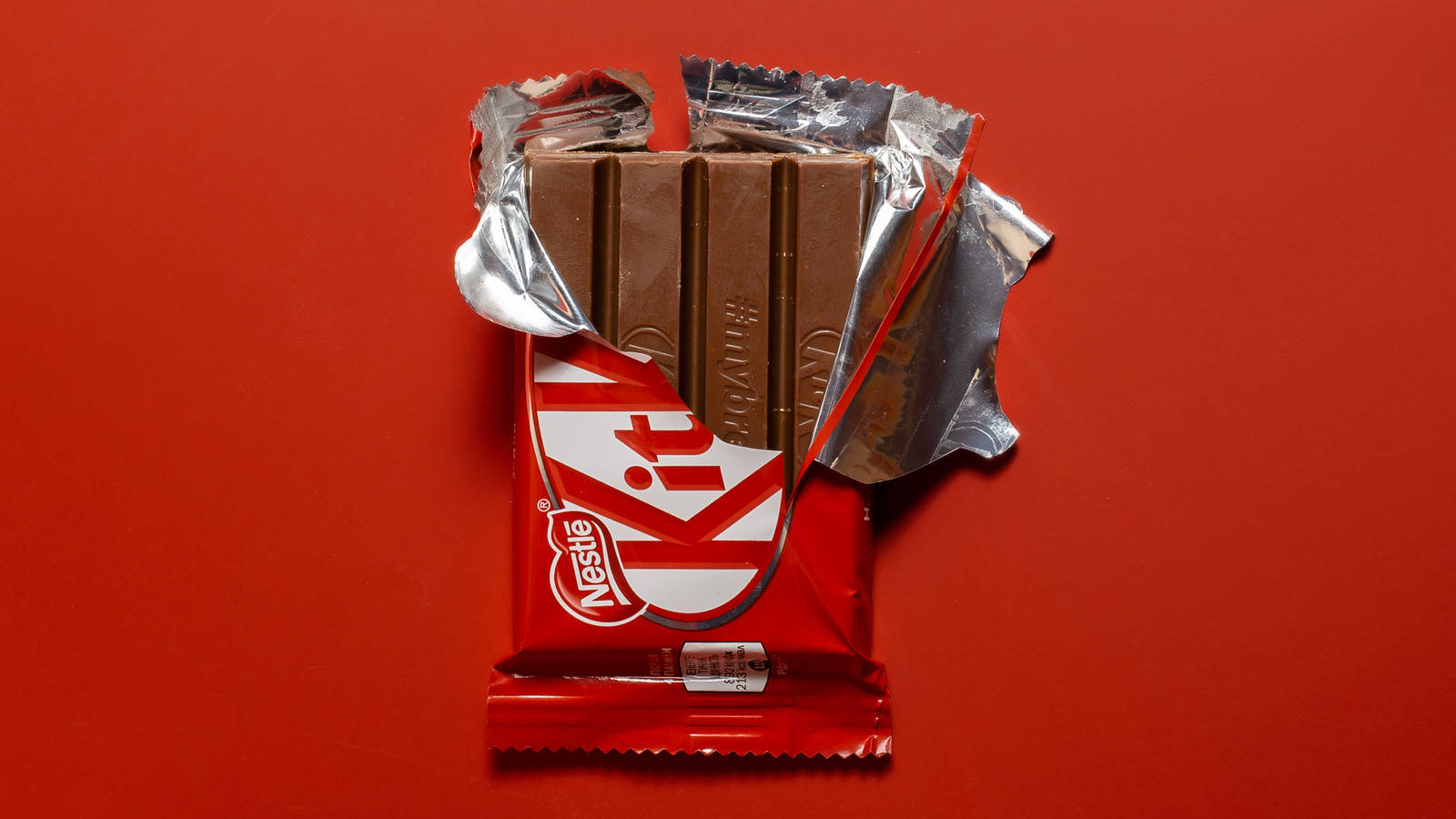 Kit Kat 開封 壁紙 — 一條部分打開的 KitKat 朱古力棒，帶有銀色錫紙，襯托在鮮紅色背景上。