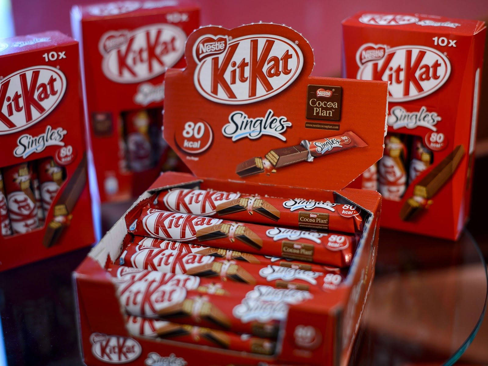 KitKat 單支裝 壁紙 — 玻璃表面上展示的紅色KitKat Singles盒裝，內有獨立包裝的朱古力條。