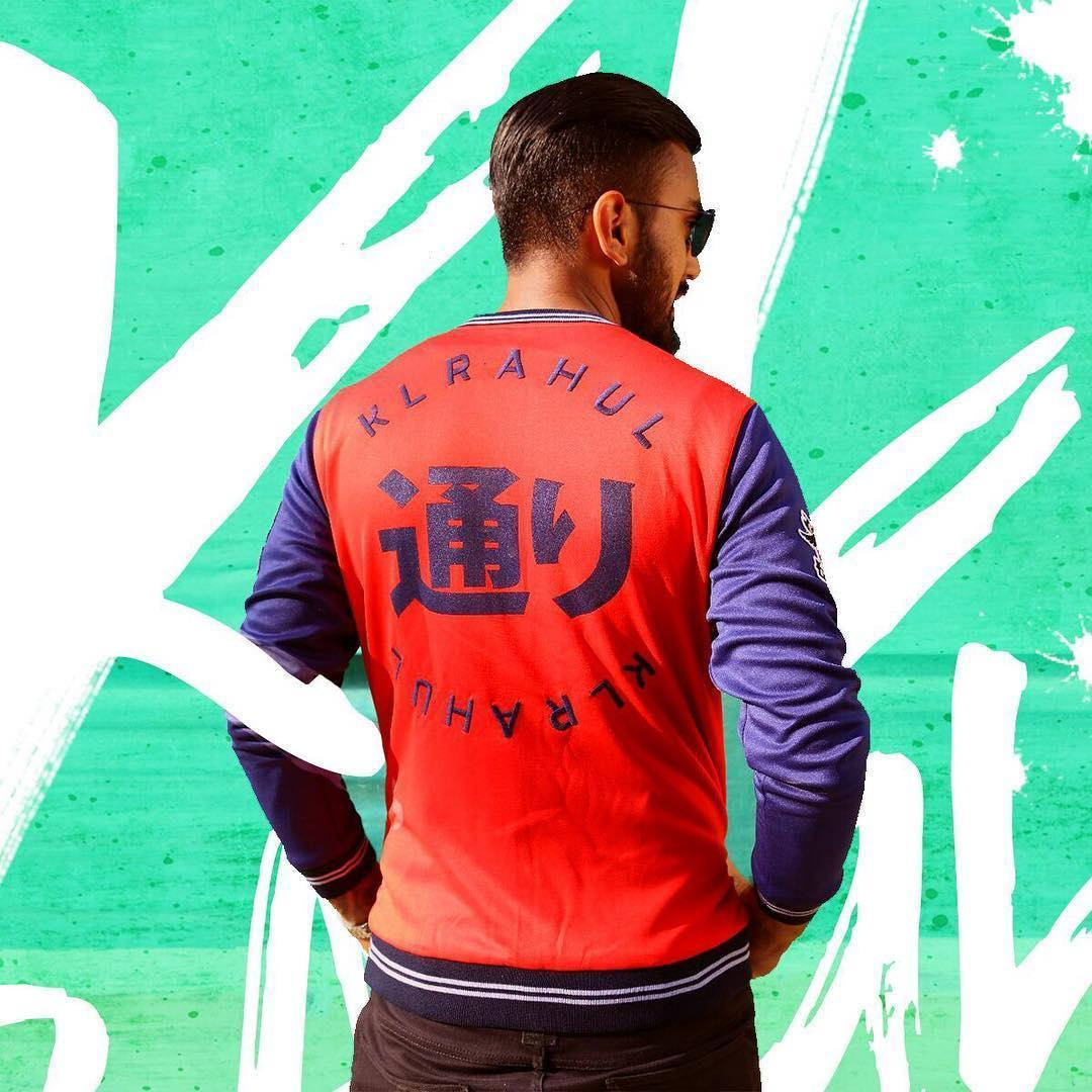 KL Rahul 穿著紅色合身校隊夾克 壁紙 — 一名身穿紅藍色棒球外套、帶有日文字的男子背對鏡頭，站在充滿活力的綠色和白色塗鴉牆前。