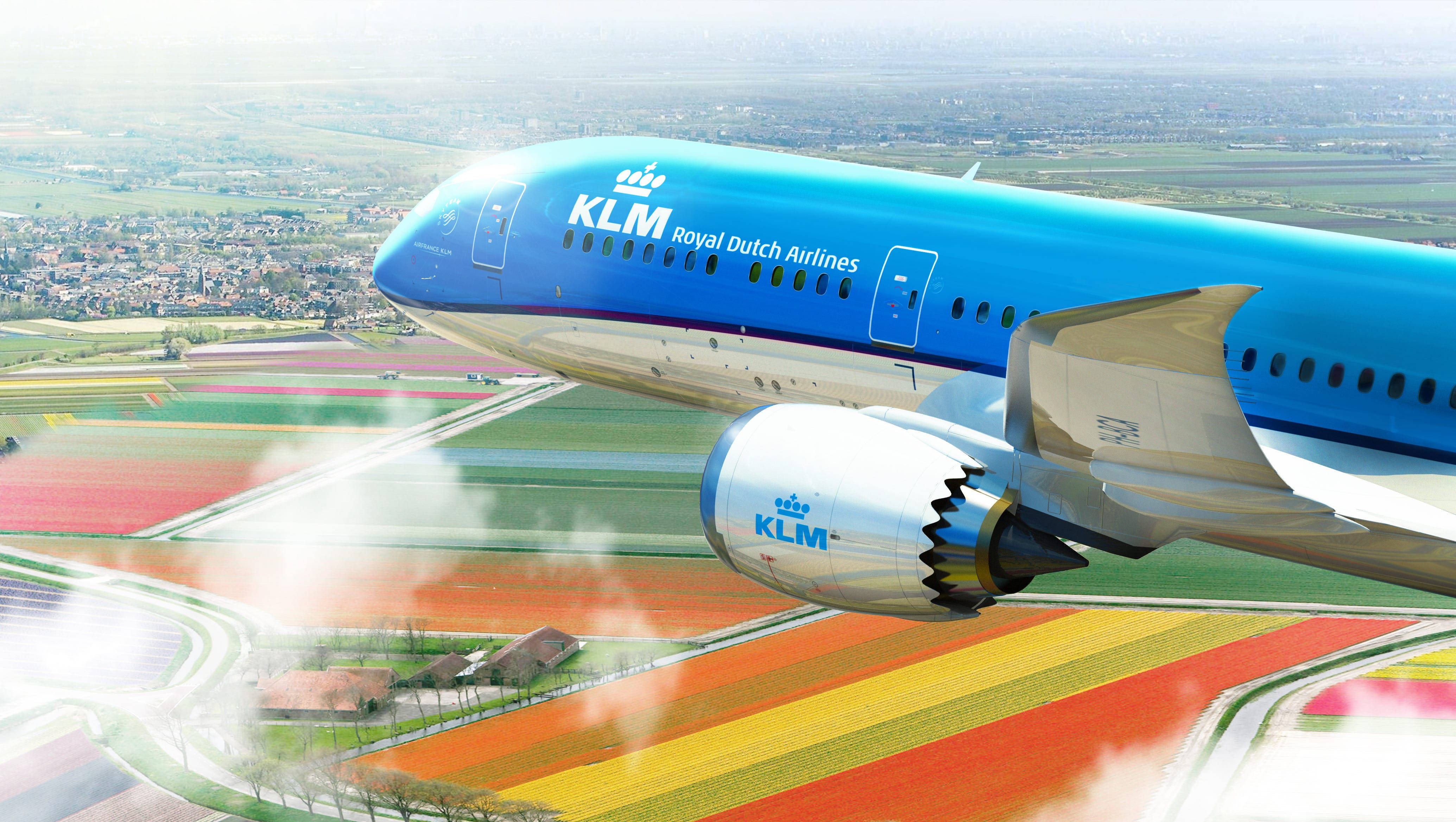 KLM 客機翱翔於美麗農場上空 壁紙 — 一架荷蘭皇家航空 KLM 客機在明亮的日光下，翱翔於色彩斑斕的鬱金香花田之上。