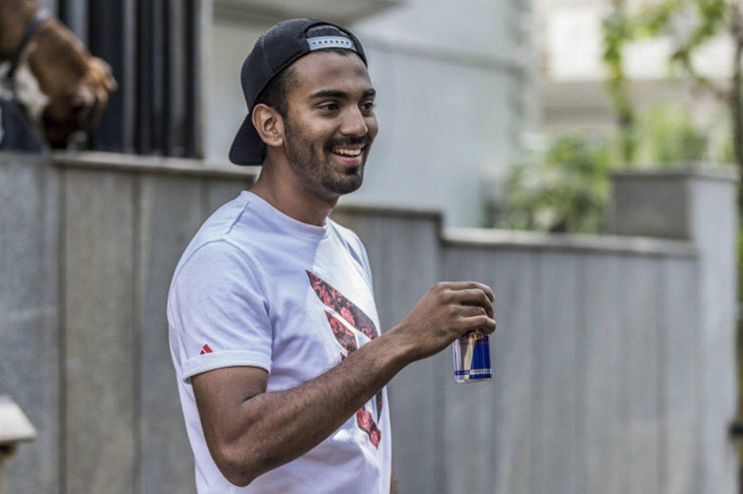 KL拉胡爾飲用Red Bull 壁紙 — 一個微笑的男人穿著白色T恤和黑色帽子，在戶外靠近圍欄的地方拿著一罐Red Bull。