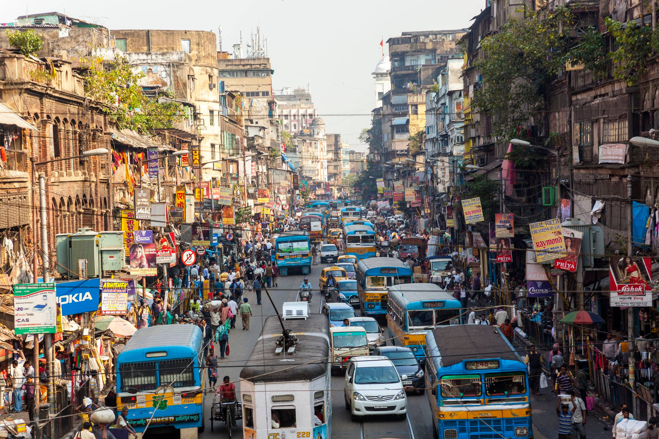 Kolkata 繁華街景 壁紙 — 繁華的都市街道，人潮、車輛和色彩繽紛的招牌充斥在風化的建築之間。