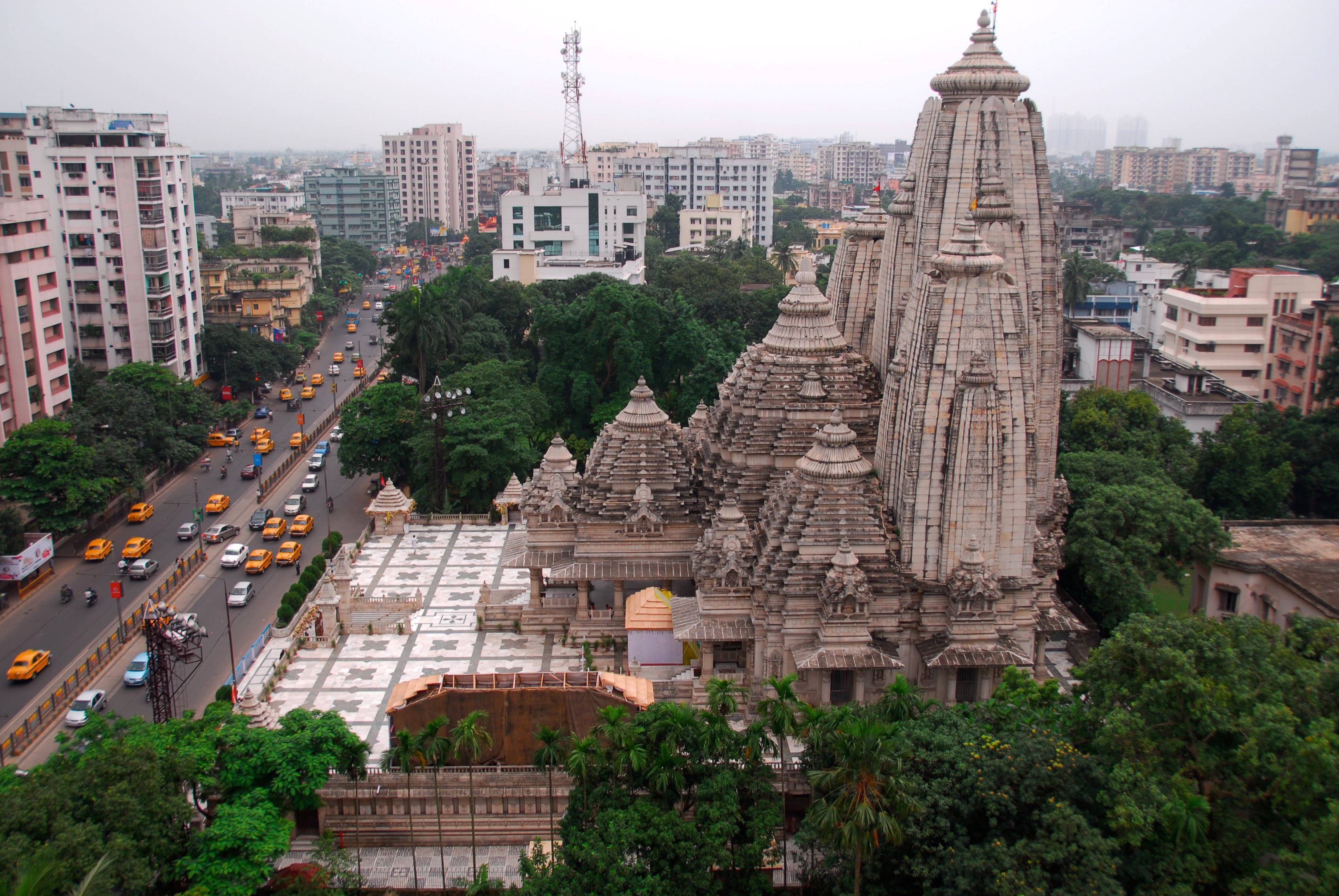 Kolkata 心臟地帶的比爾拉神廟 壁紙 — 一座宏偉的石造寺廟，擁有精緻的尖塔，聳立在充滿黃色出租車和現代建築的繁華城市街道之上。