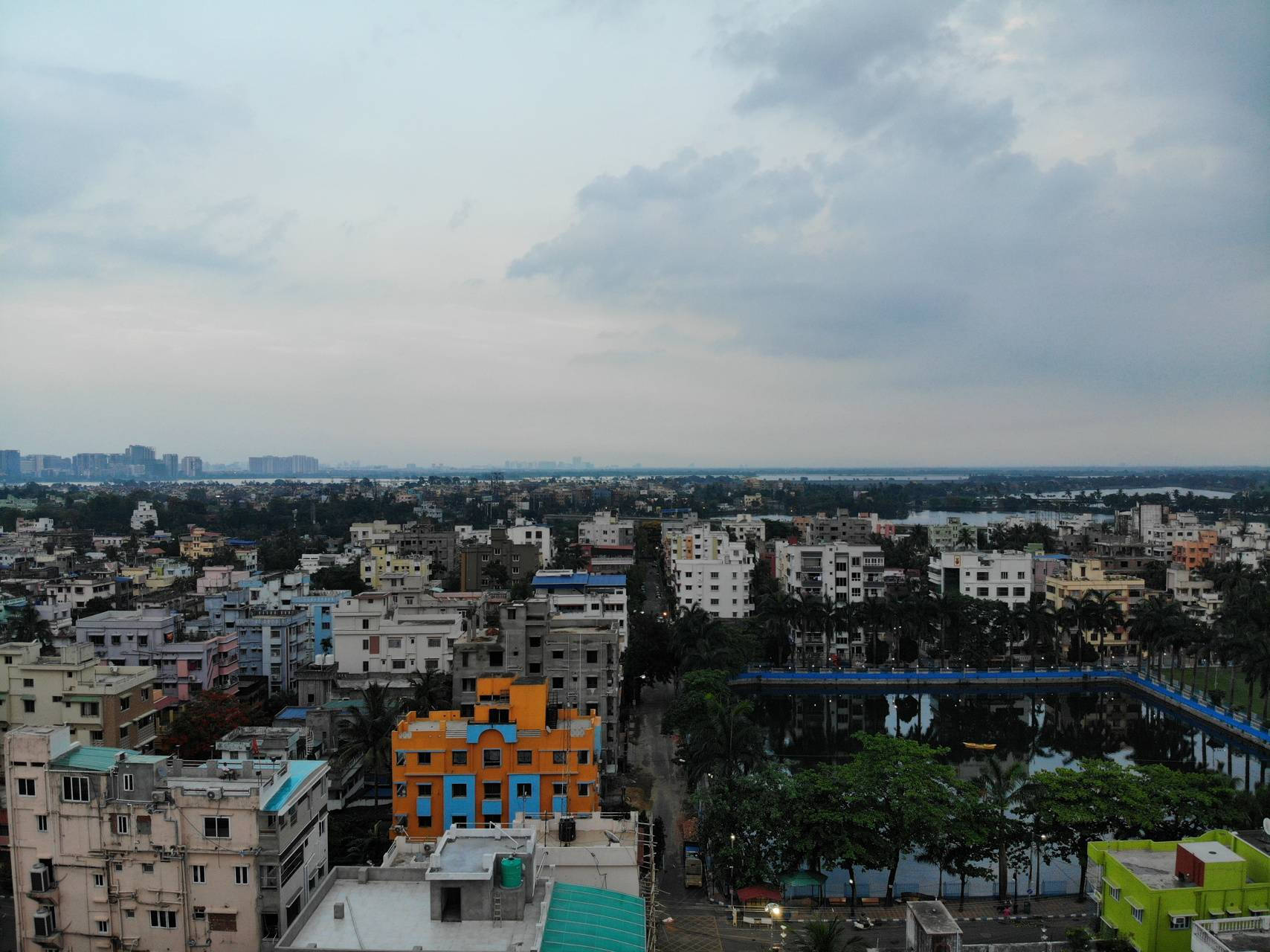Kolkata 城市天際線 壁紙 — 多雲天空下，色彩繽紛的建築物和反射水體構成的廣闊城市景觀。