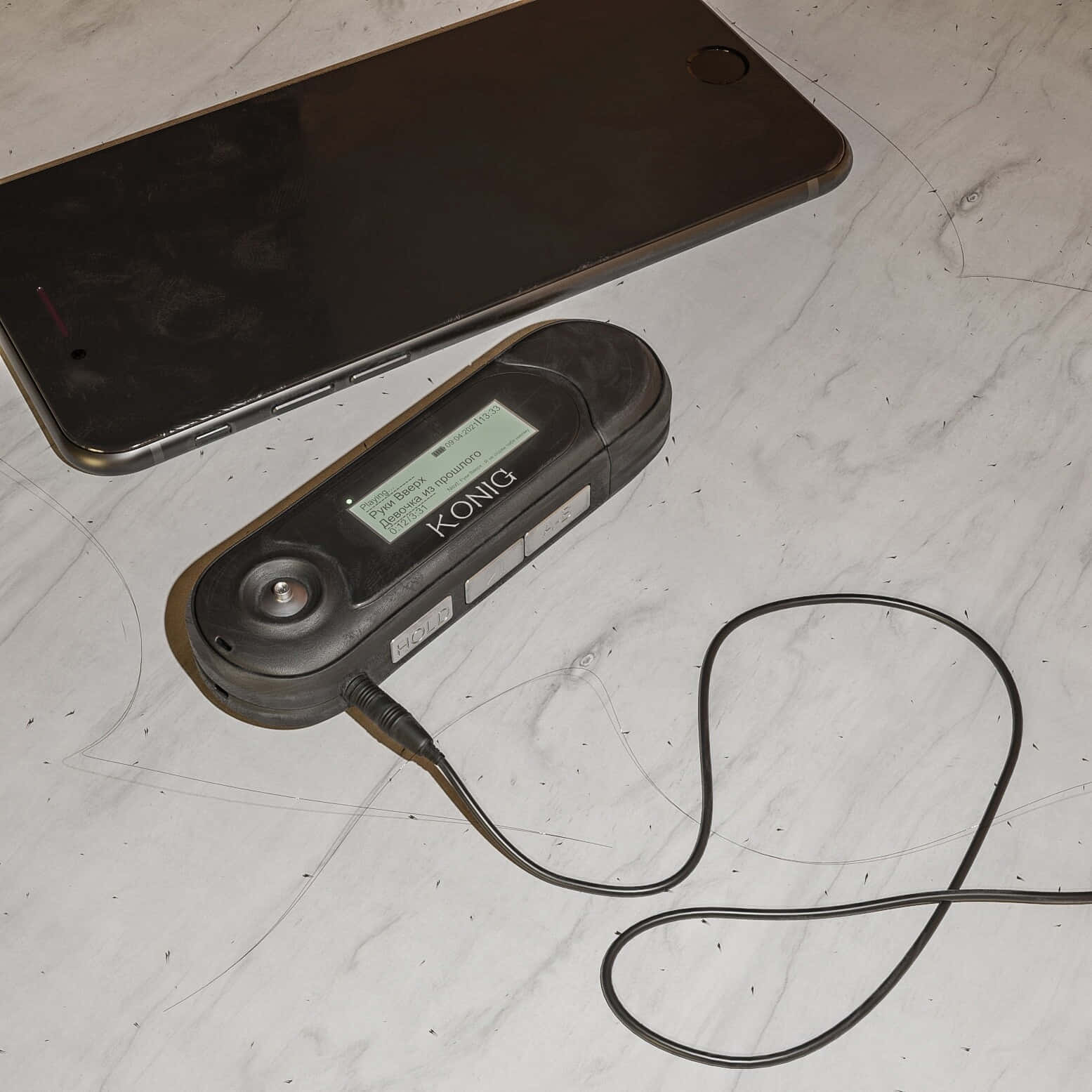 Konig MP3播放器圖片 壁紙 — 一部黑色Konig測光錶和智能手機放在白色大理石表面上，周圍散落著髮絲。
