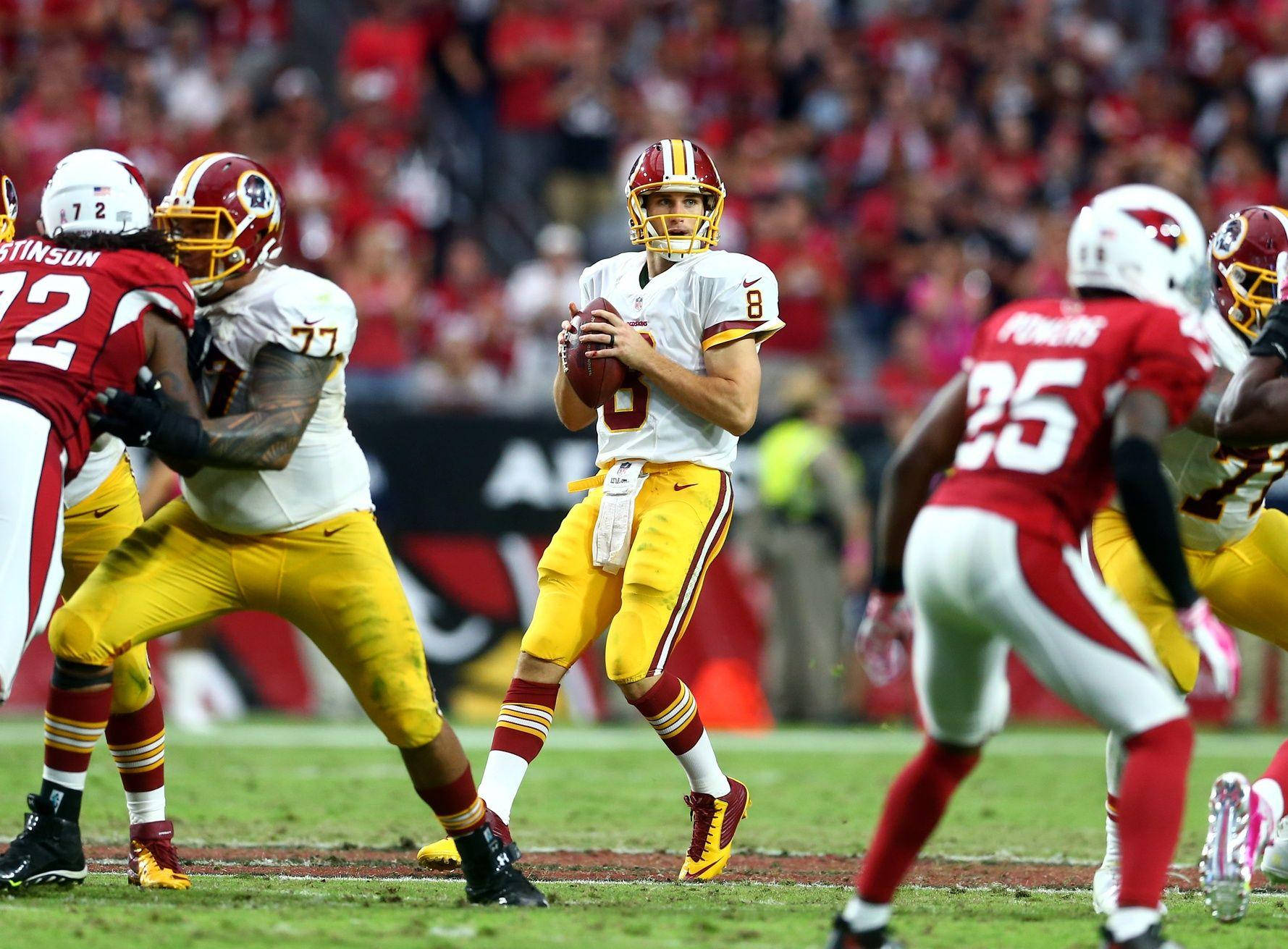 Korey Stringer 保護 Kirk Cousins 壁紙 — 一名身穿白色和金色制服的美式足球四分衛在比賽中與隊友和對手一起準備投球。