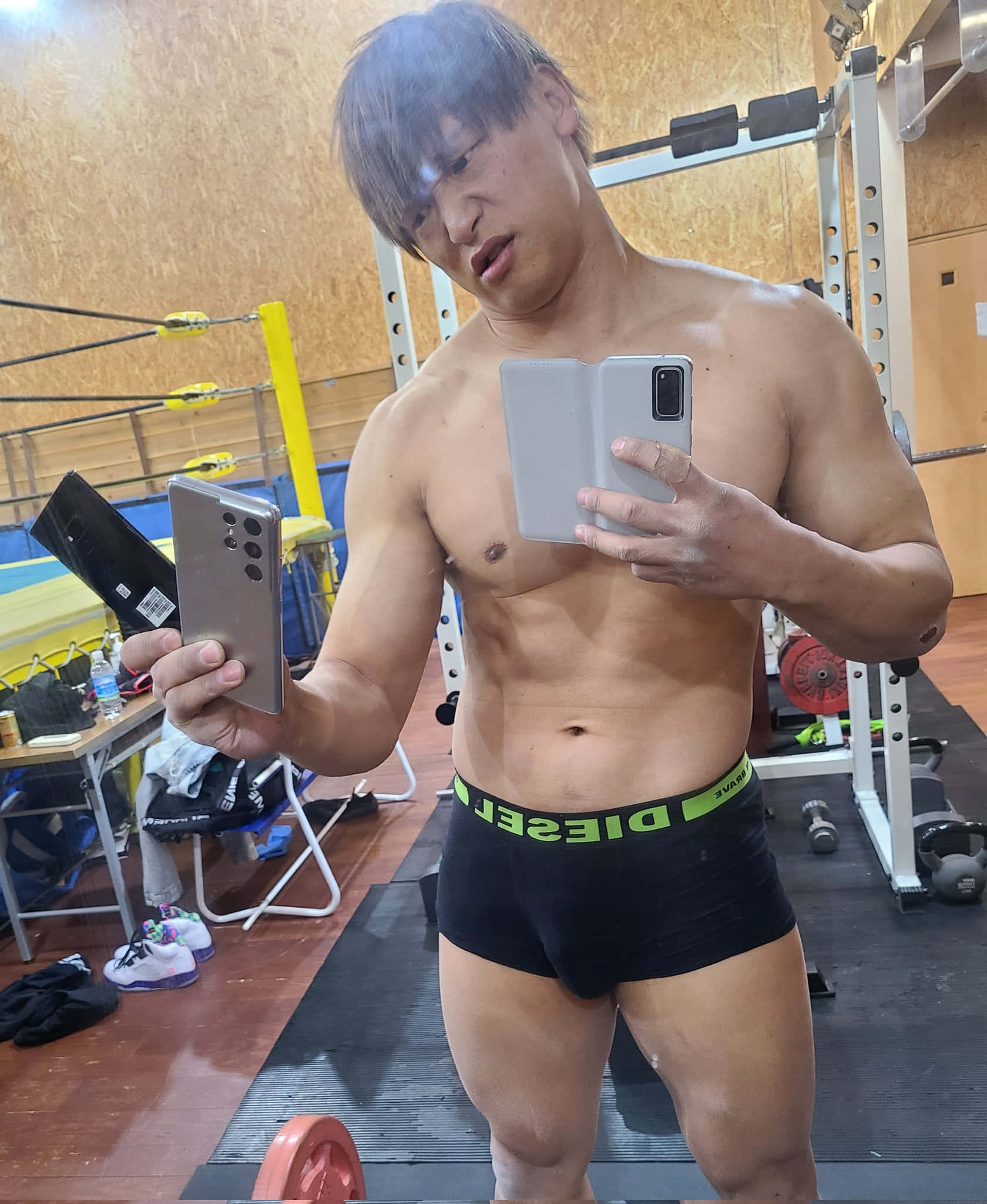 Kota Ibushi 在健身房自拍 壁紙 — 一個肌肉發達的男人穿著黑色Diesel內褲，在健身房拿著兩部智能手機對著鏡子自拍。