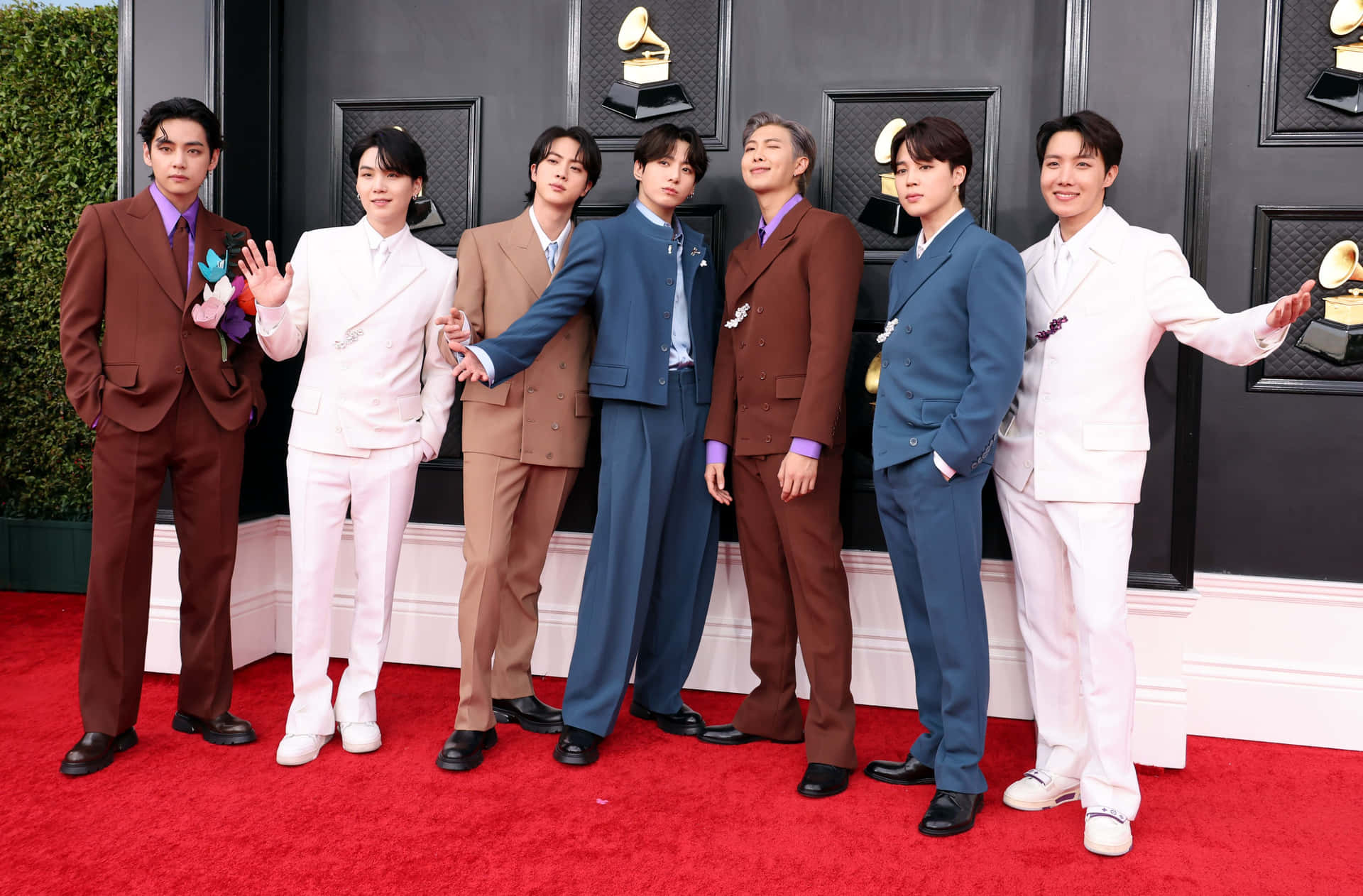 KPOP BTS 紅毯照片 壁紙 — 七位時尚男士穿著訂製西裝，在黑色牆壁前的紅地毯上自信地擺姿勢，旁邊有格林美獎盃。