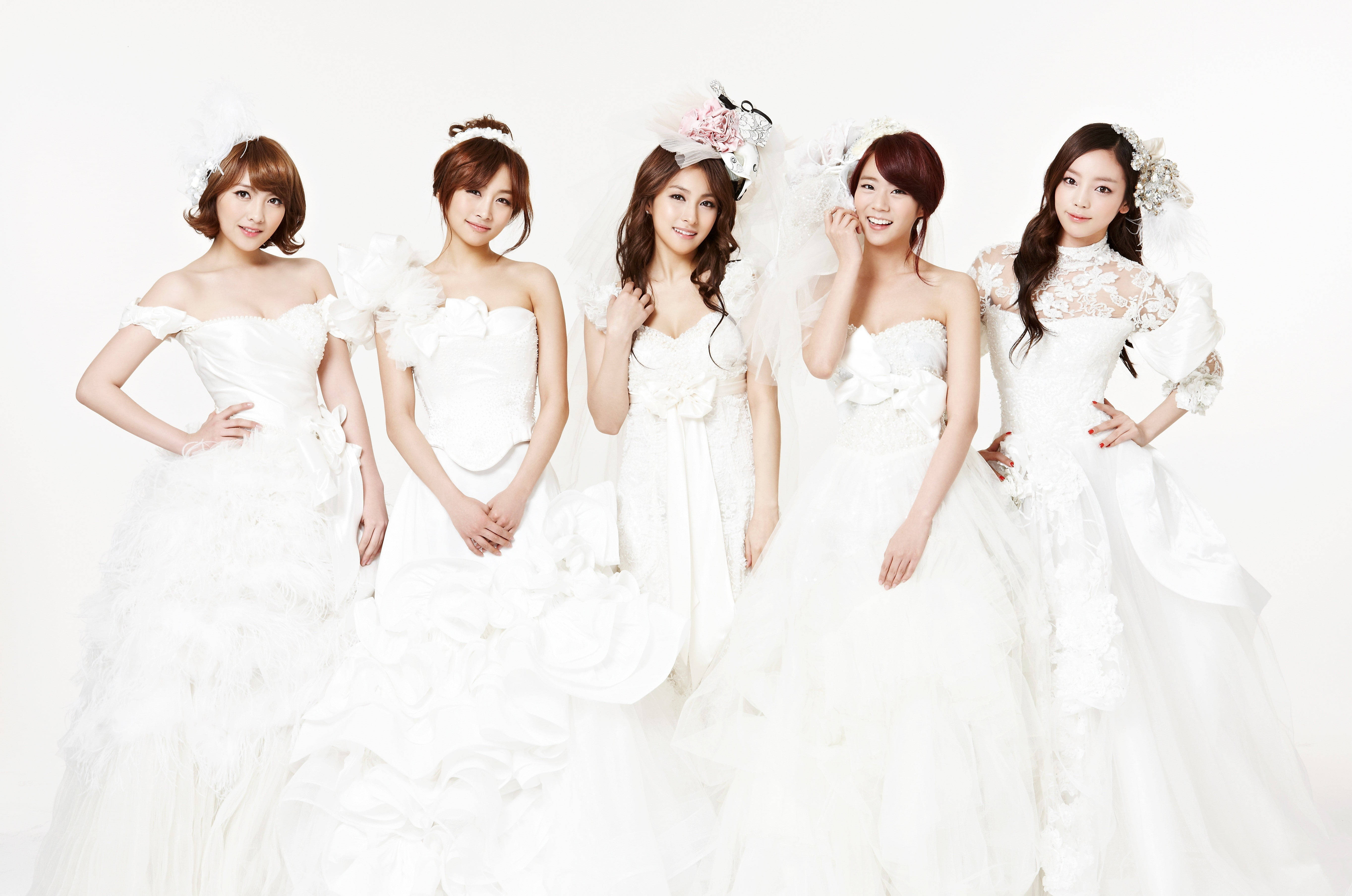 Kpop 婚紗 壁紙 — 五位身穿精緻白色婚紗的女性在柔和的燈光下，在純白色背景前優雅地擺姿勢。